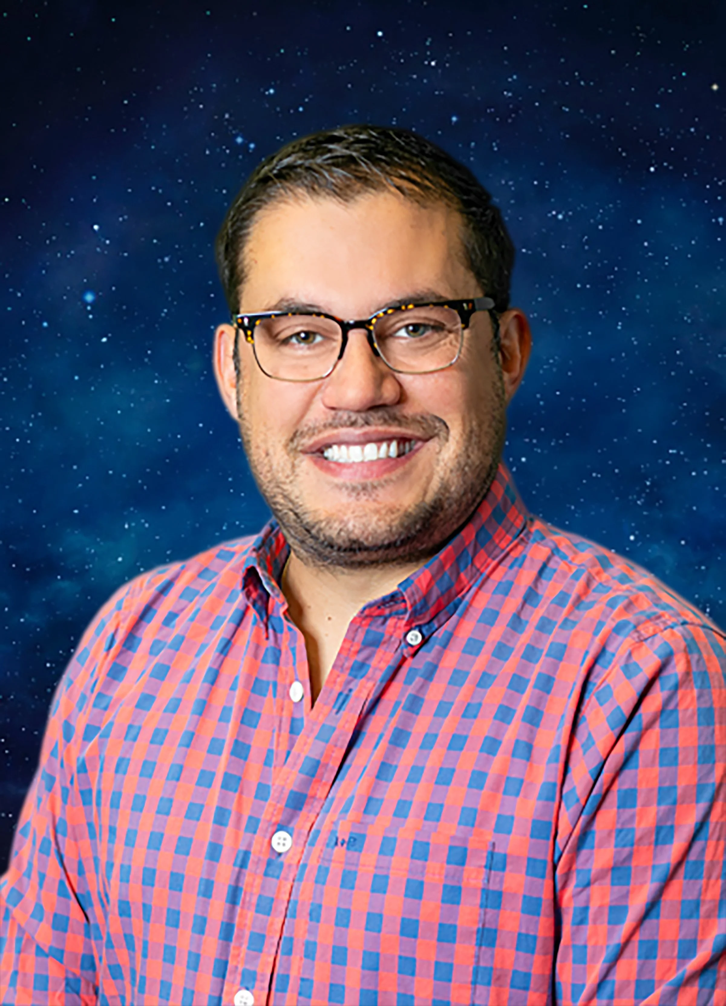 Headshot of a man with glasses, smiling, wearing a red and blue checkered shirt, against a starry night sky background for a headshot with Cannonfire Photography in Orlando.
