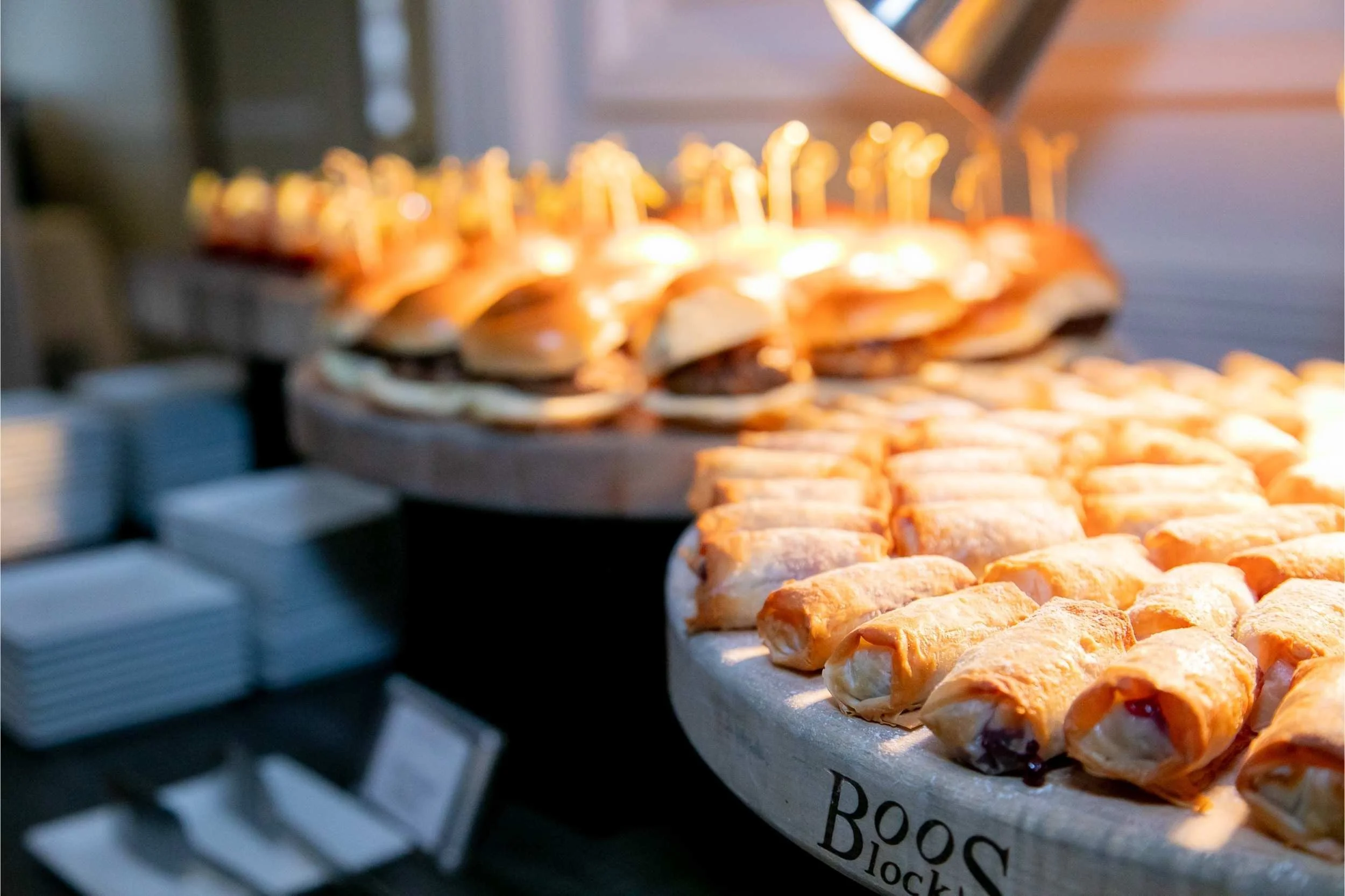 A display of assorted pastries and sandwiches on a buffet table, with plates stacked on the side.