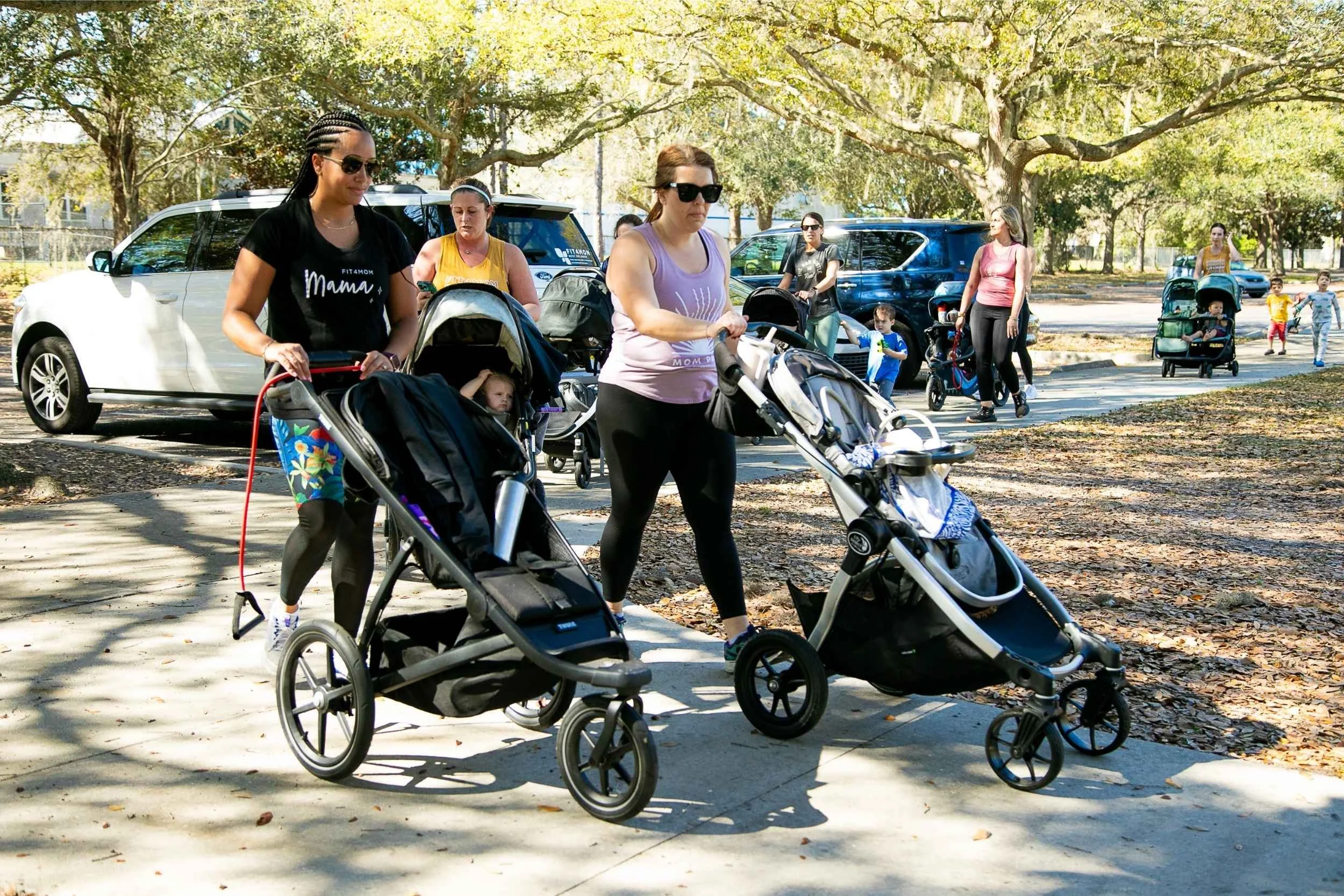Multiple women pushing strollers with children in a park on a sunny day, with other families and children in the background for an advertising photography session by Cannonfire Photography in Winter Garden.