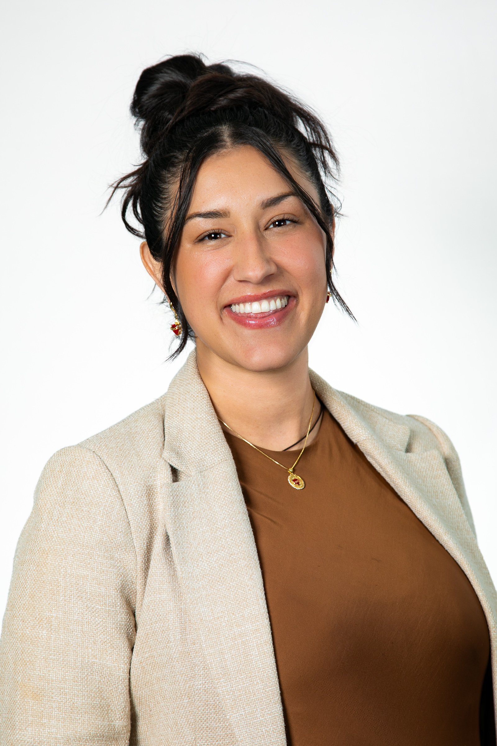 A woman smiling with dark hair tied up, wearing a beige blazer, brown top, and jewelry, against a plain white background for a headshot with Cannonfire Photography in Orlando.