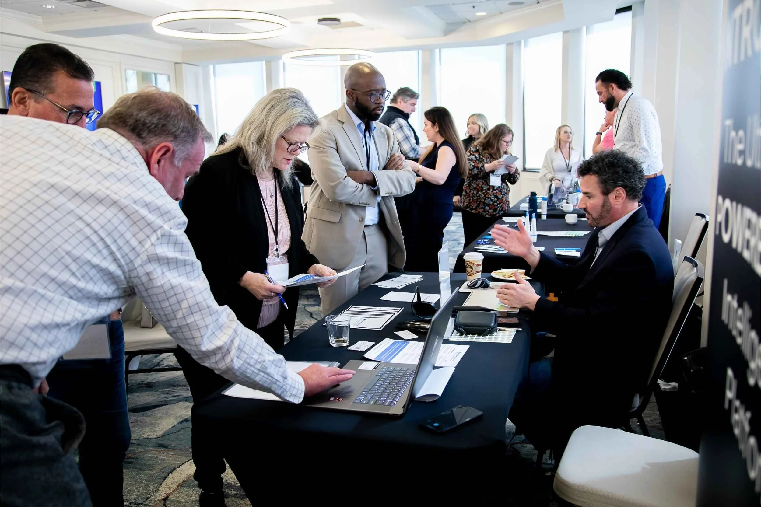 People standing and sitting around a table at a conference or business event, engaging in conversation and examining materials for a conference photographed by Cannonfire Photography in Orlando.