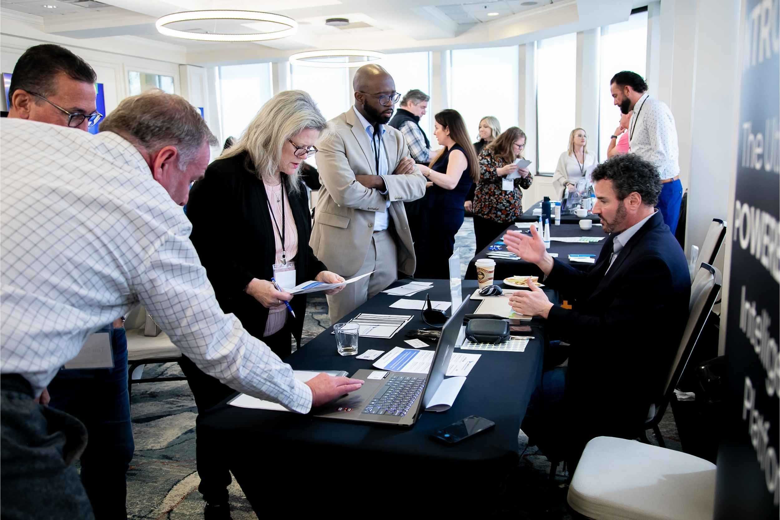 People standing and sitting around a table at a conference or business event, engaging in conversation and examining materials for a conference photographed by Cannonfire Photography in Orlando.