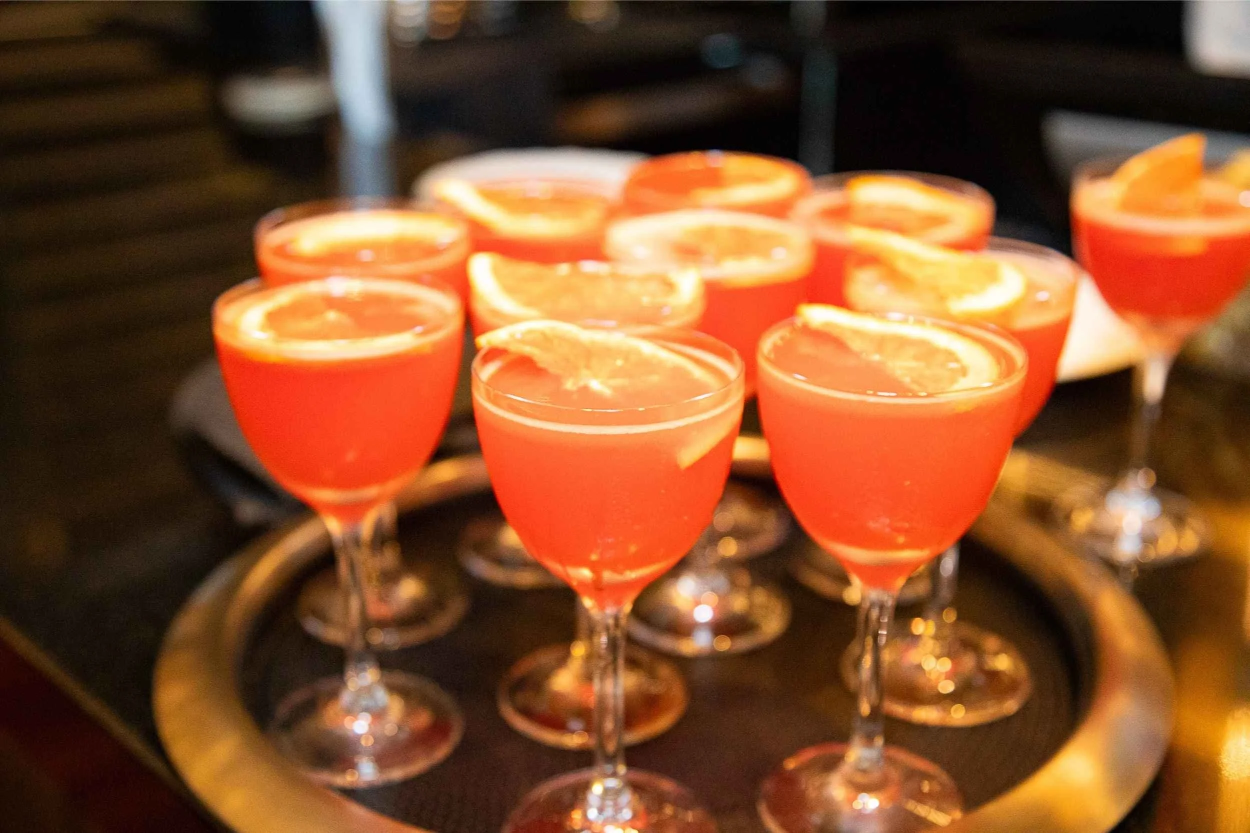 Several pink cocktails garnished with orange slices on a tray.