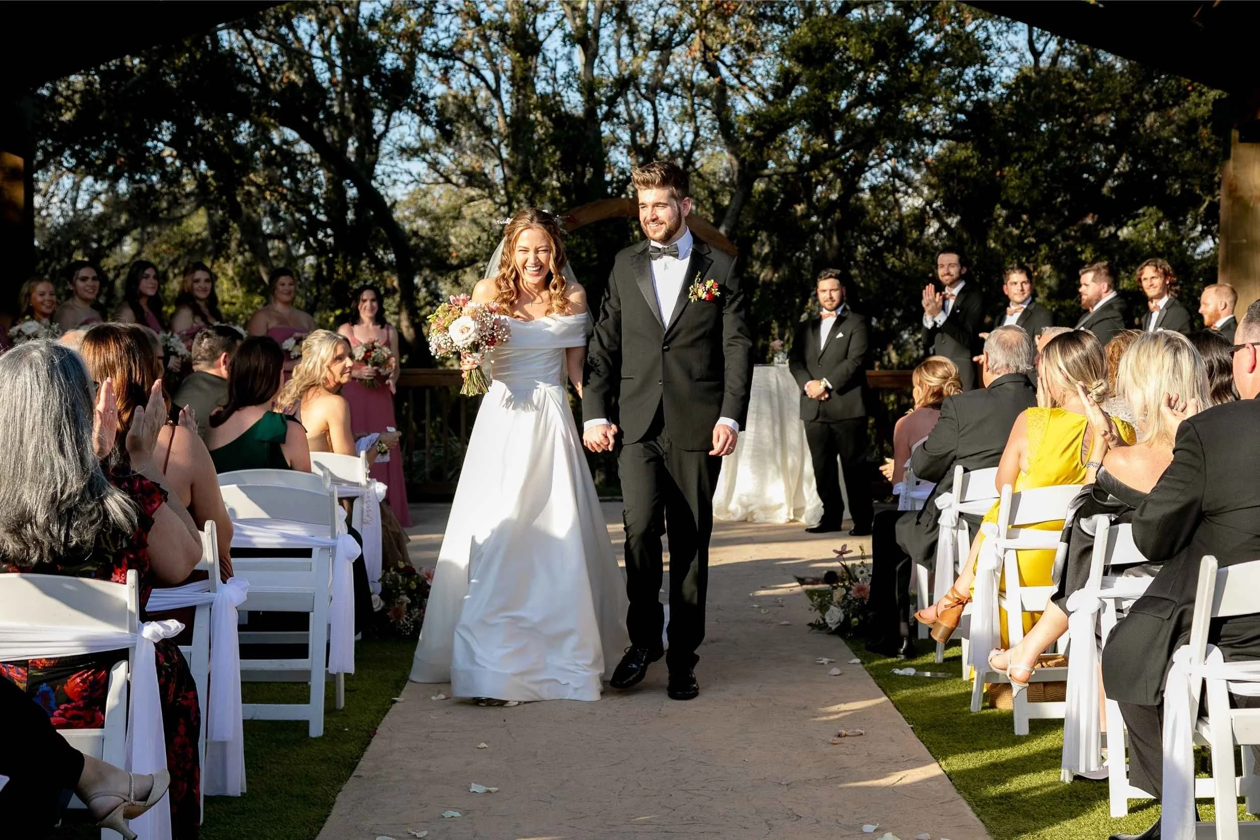 Bride and groom walking down the aisle at their outdoor wedding ceremony, surrounded by seated guests and bridesmaids in the background for a wedding photographed by Cannonfire Photography.