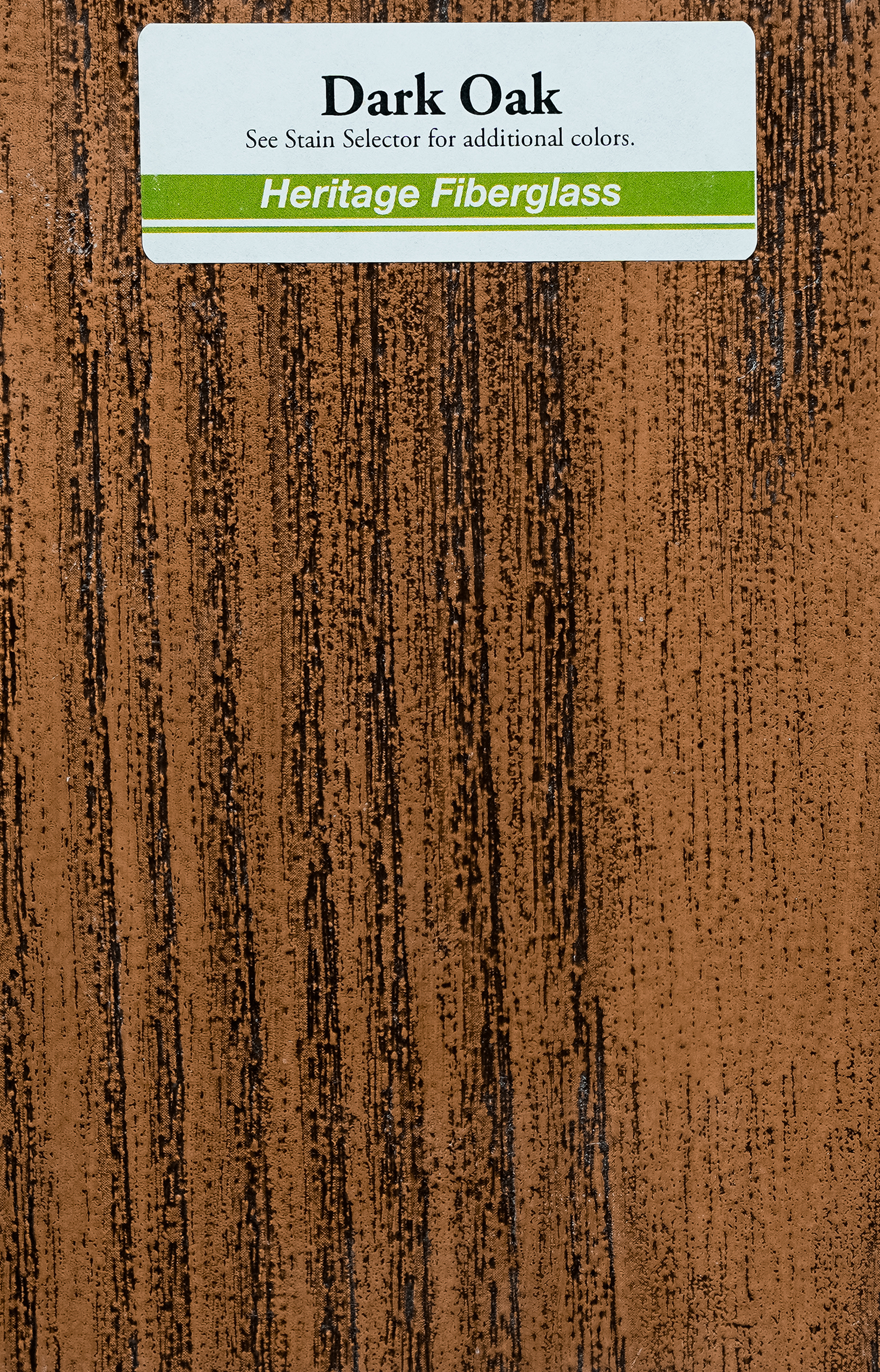Close-up of a wood grain sample labeled as Dark Oak, part of Heritage Fiberglass collection, with a sticker indicating to see the stain selector for additional colors.