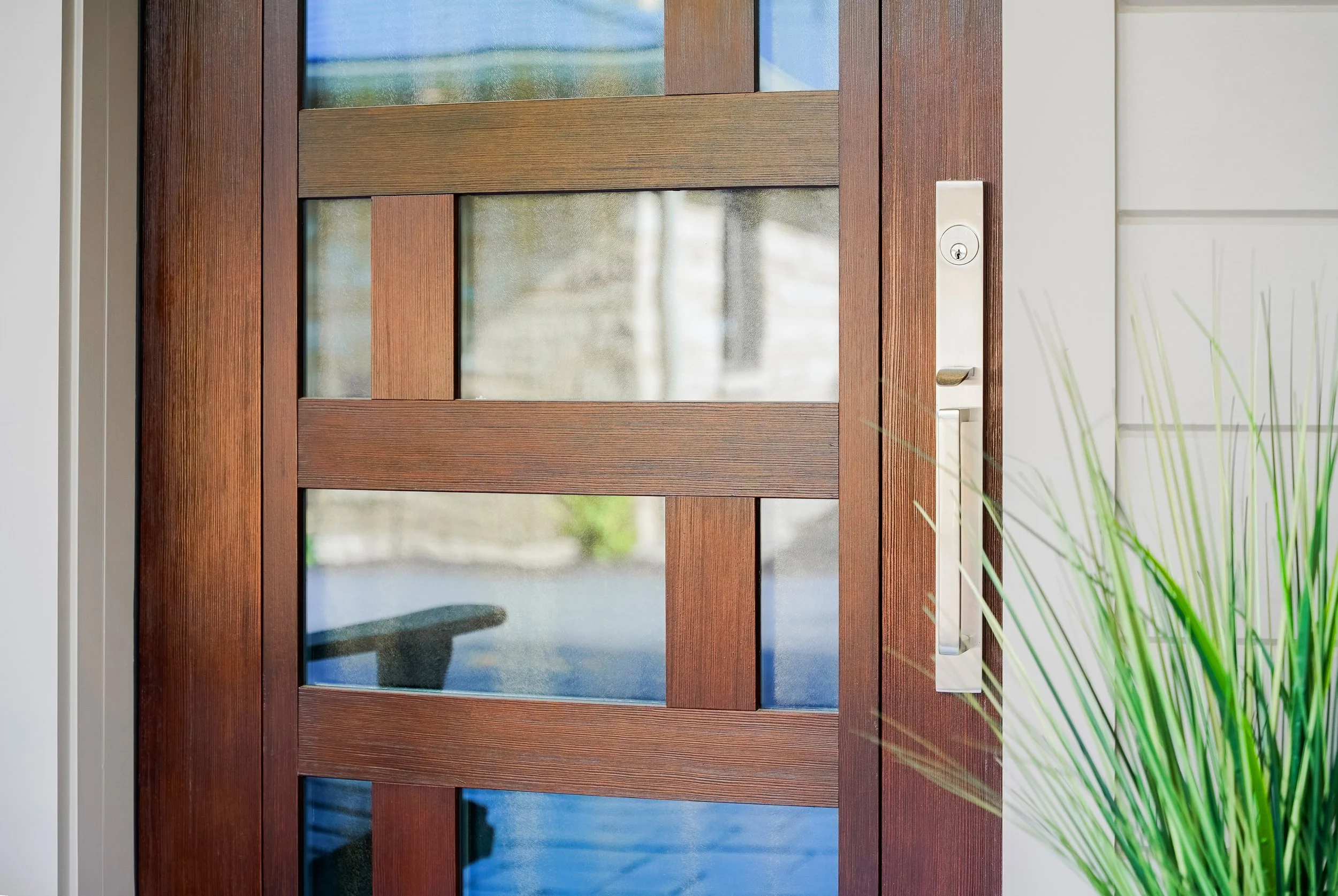 Close-up of a wooden front door with glass panels and a silver door handle.