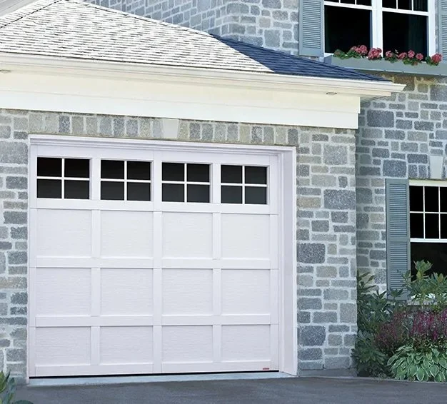 Close-up view of a white garage door on a house with gray stone exterior and a small window with flower box above.