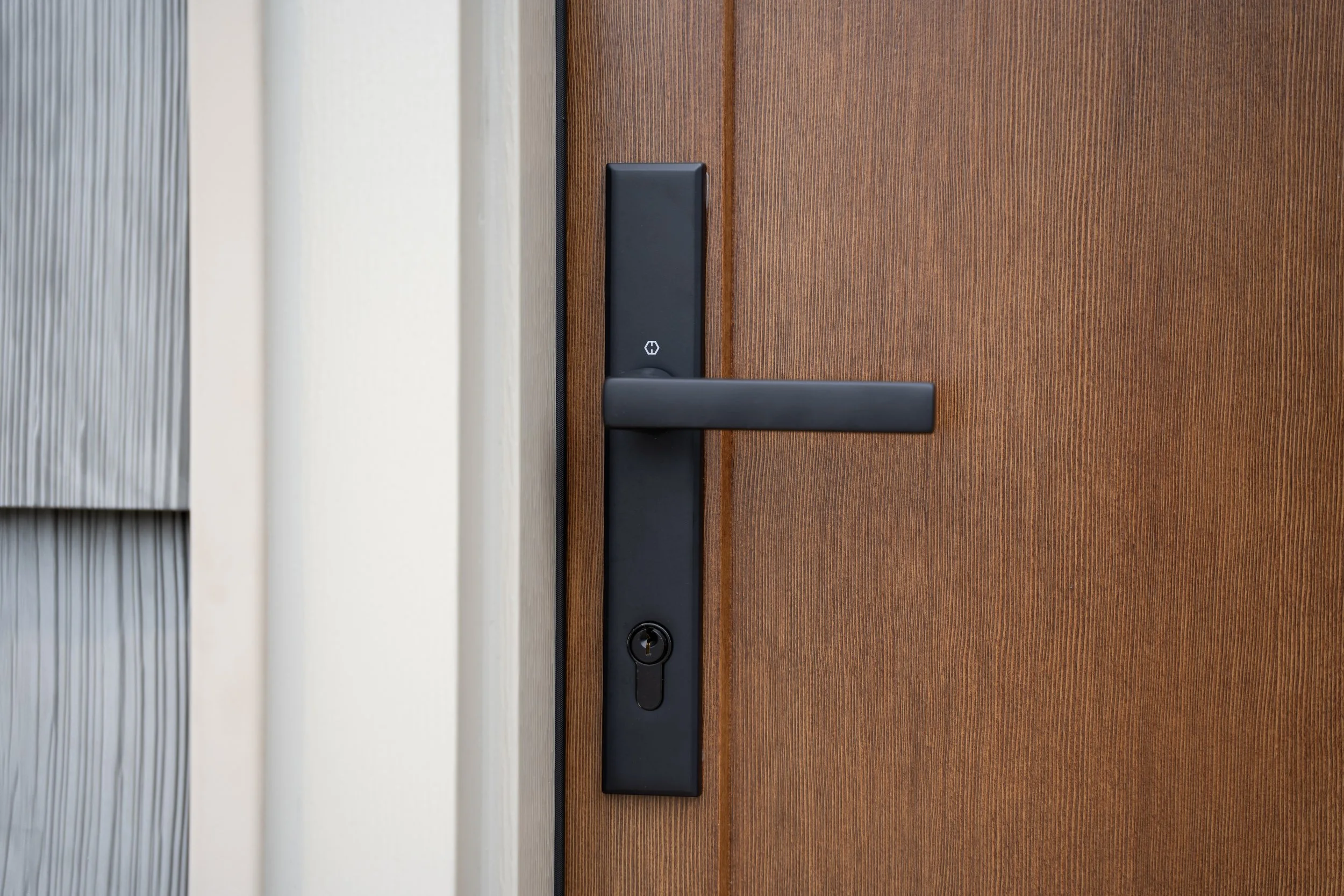 Close-up of a modern black door handle and lock on a wooden door with a vertical wood grain pattern.