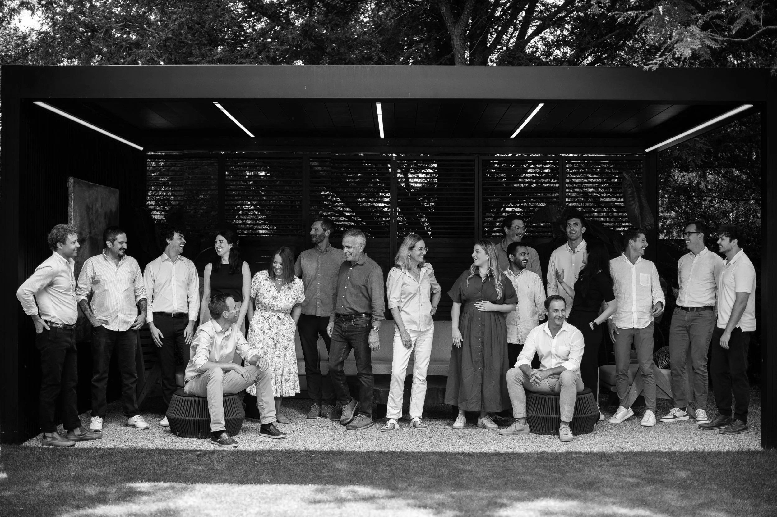 A black-and-white photo of a diverse group of coworkers standing and sitting outdoors, smiling and engaging with each other.
