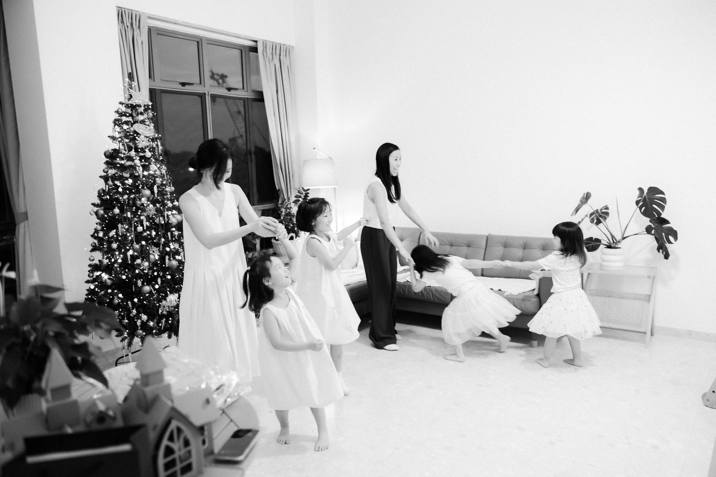 A group of women and children playing tug of war during Christmas celebration in a living room decorated with a Christmas tree. Family Photography. Family Photoshoot at home. Singapore Family Photography.