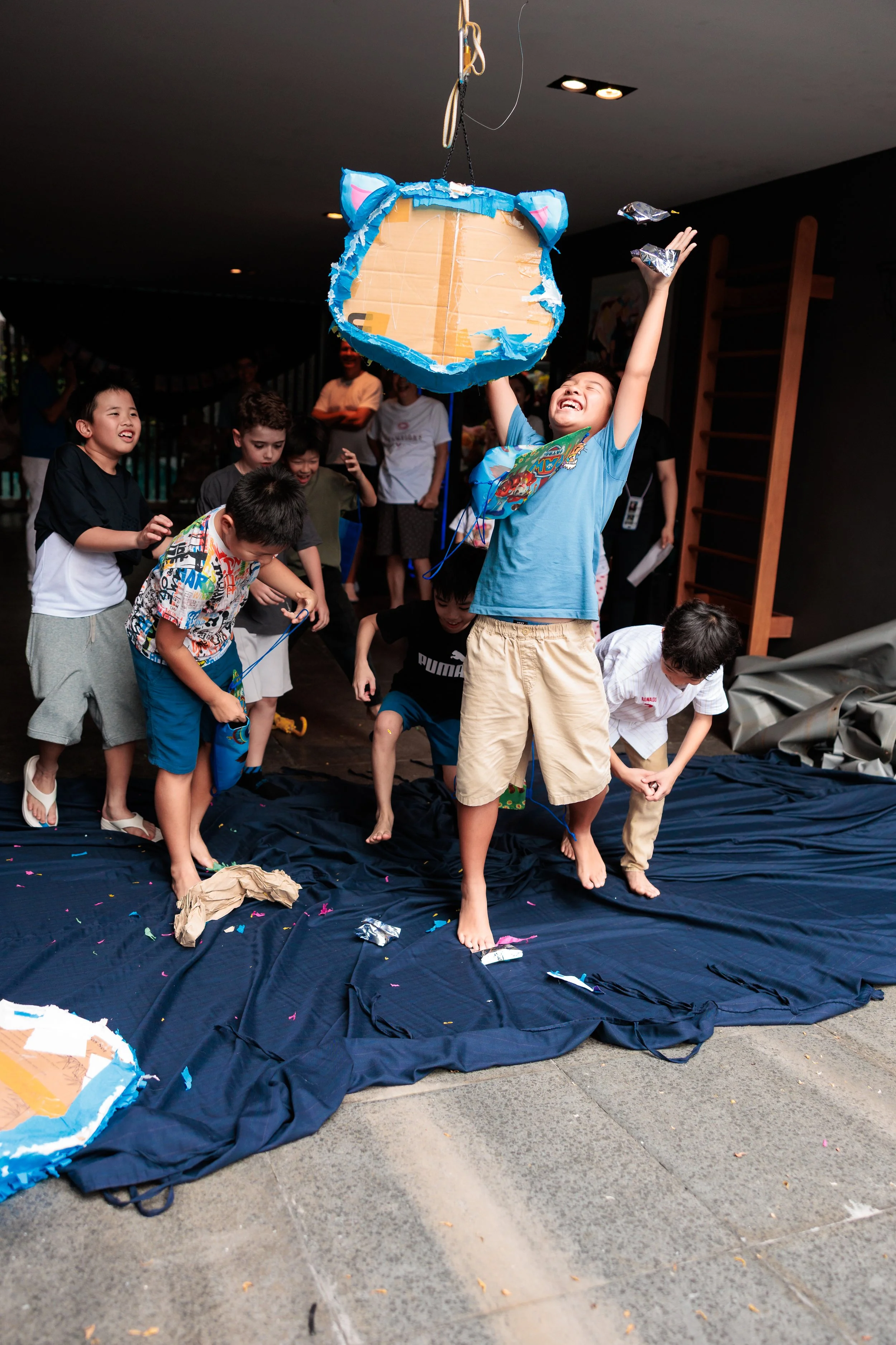 Children at a birthday party playing a game with a piñata, with some children taking turns hitting it and others watching and cheering. KPOP Demon Hunter Theme. Singapore Family Photography. Family Photoshoot at home. Singapore Birthday Photography.