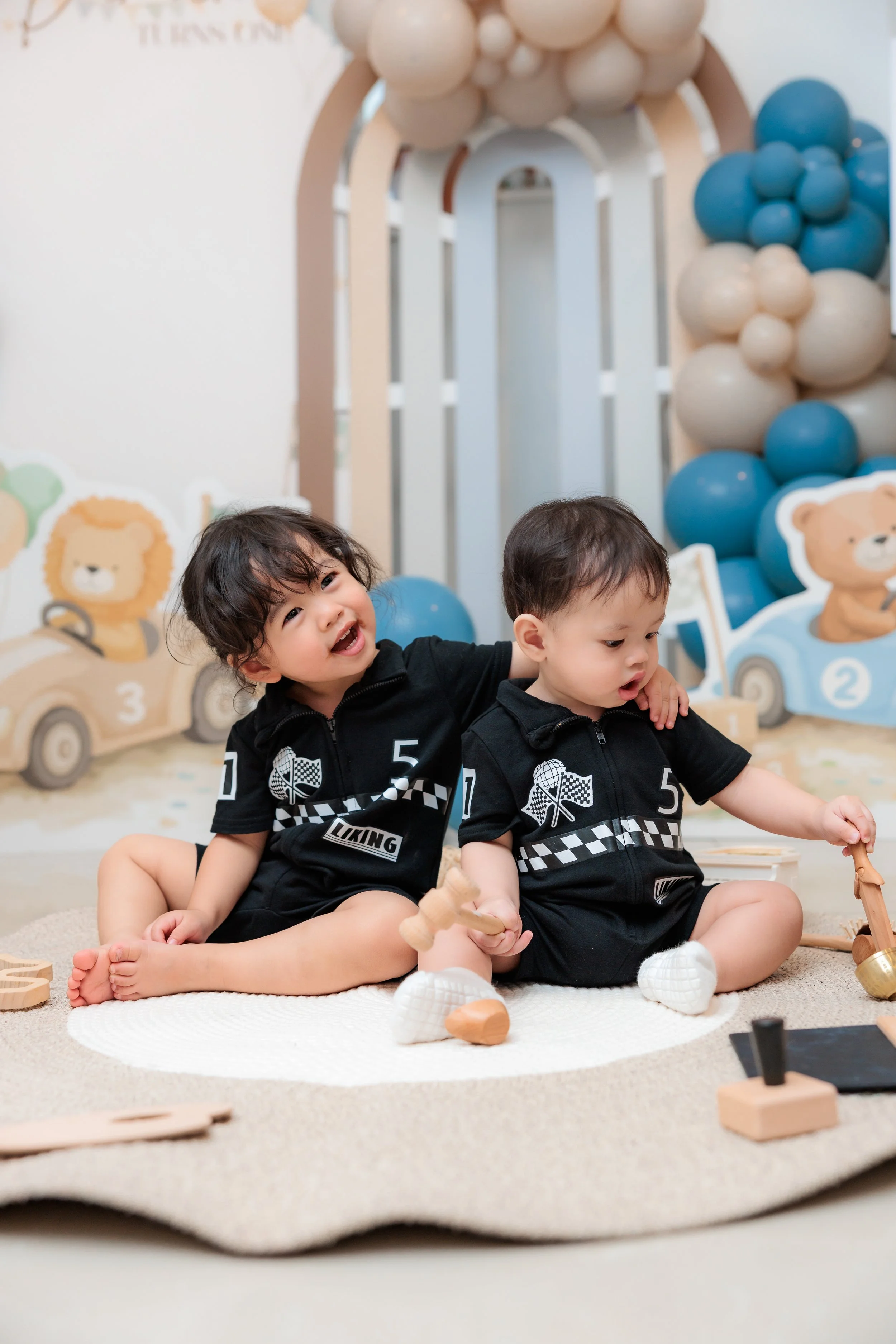 Two young children sitting on a beige rug in a playroom with lion-themed wall decorations and balloon art, playing with wooden toys. Family Photography Session. Birthday Photography Session. Event Photography.