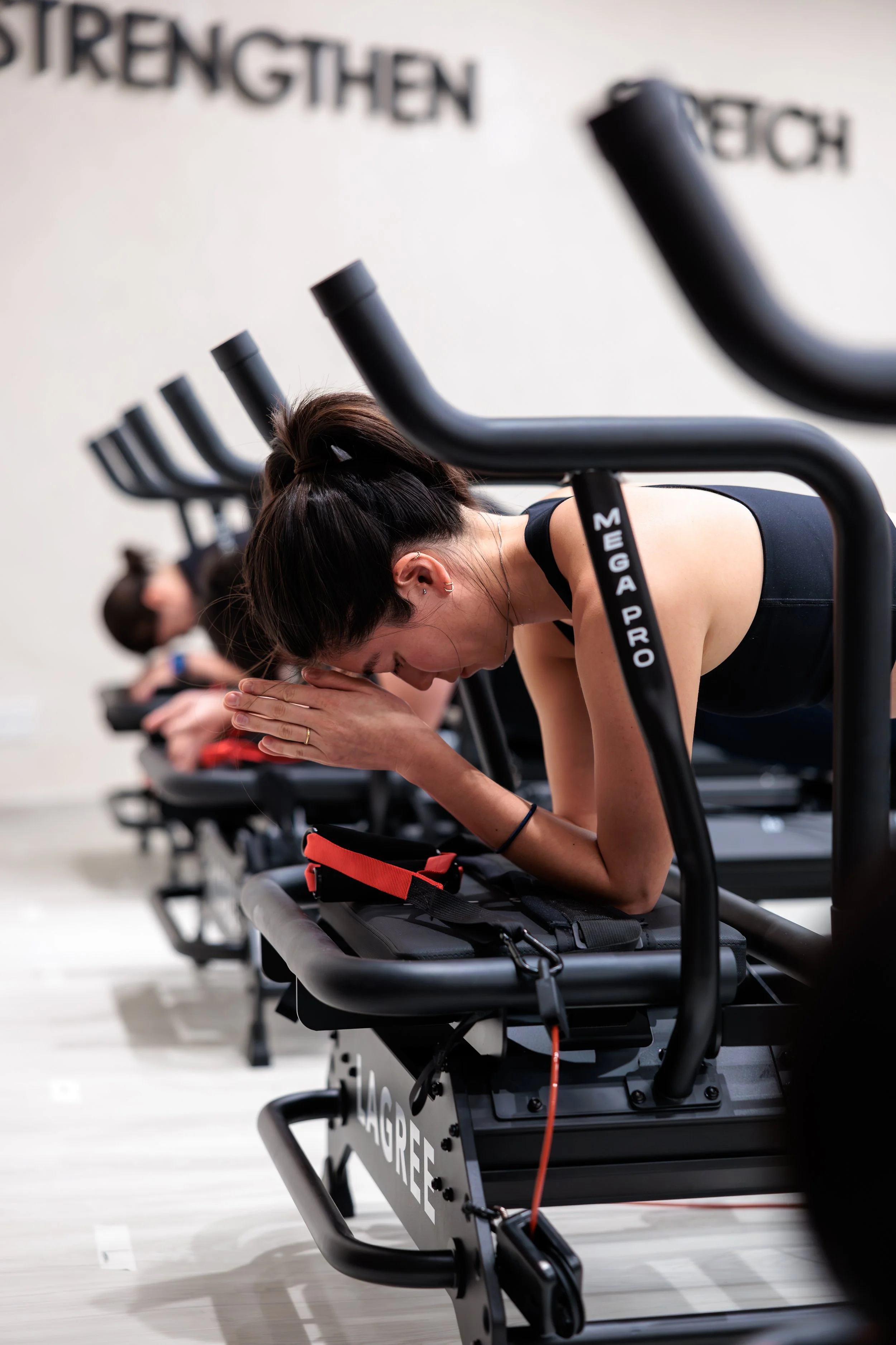 Women doing Pilates on reformer machines in a fitness studio, focusing on stretching and relaxation. HKore Megaformer Lagree Yoga Studio Photography