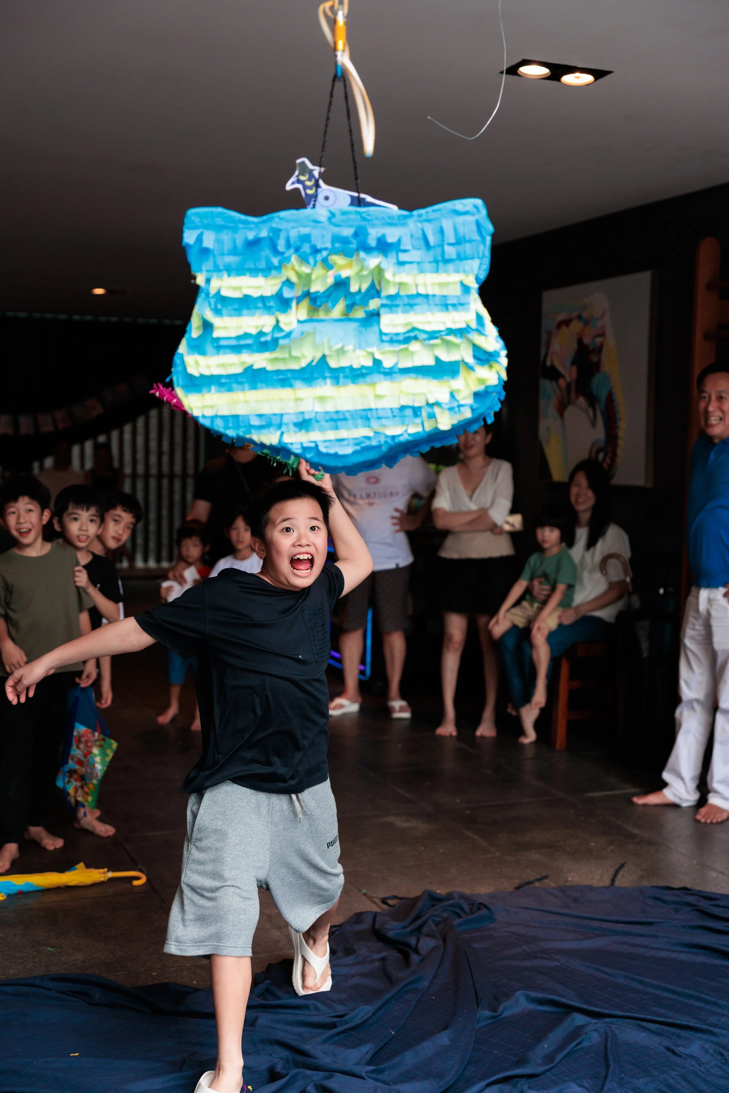 A young boy excitedly runs towards a colorful piñata hanging from the ceiling during a celebration, Singapore Birthday photography. Family Photography. Family Photoshoot at home. Singapore Family Photography. 