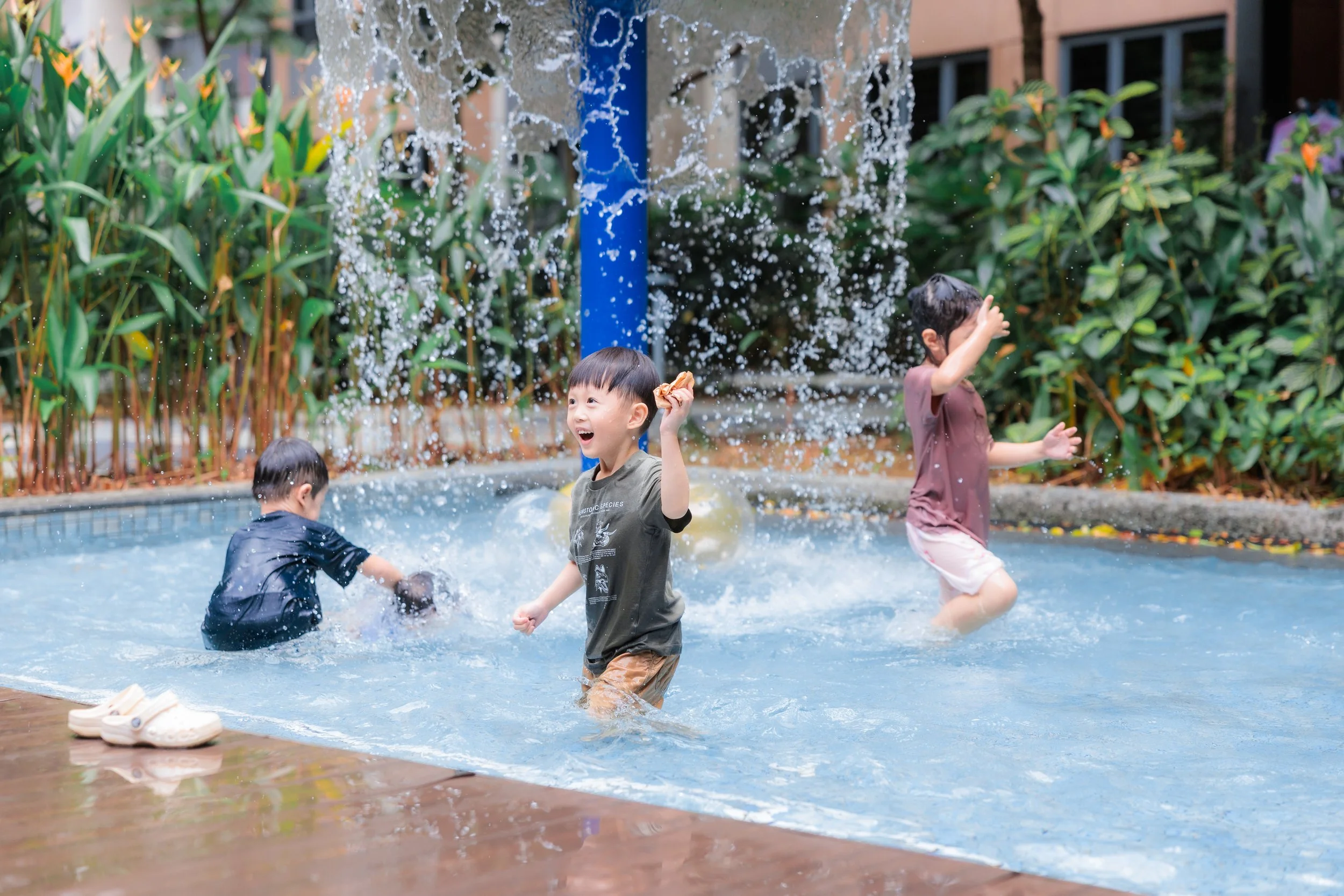 Children playing and splashing water in a swimming pool, surrounded by green bushes and plants. Family Photography Session. Birthday Photography Session. Event Photography.
