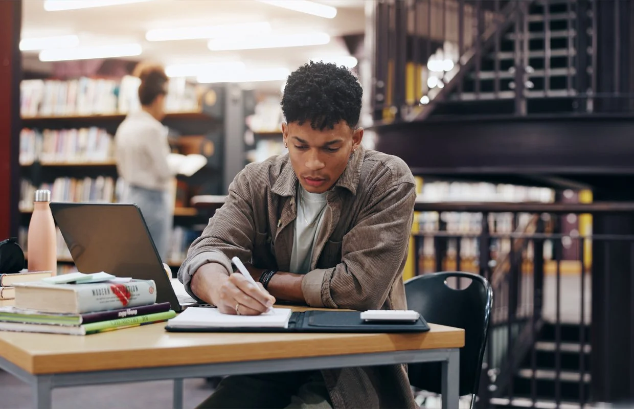 Student comparing student loan options, in library, laptop and books