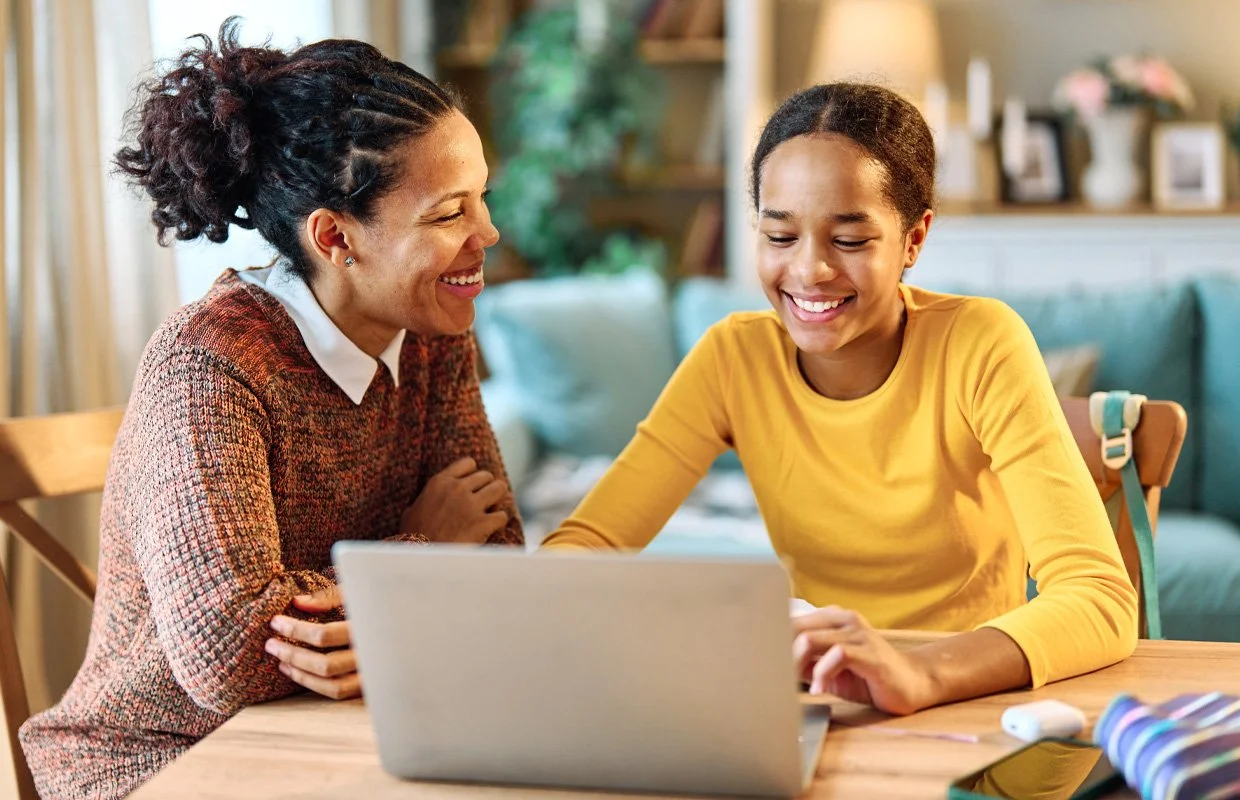 Mother and daughter, possibly, at laptop at kitchen table, smiling
