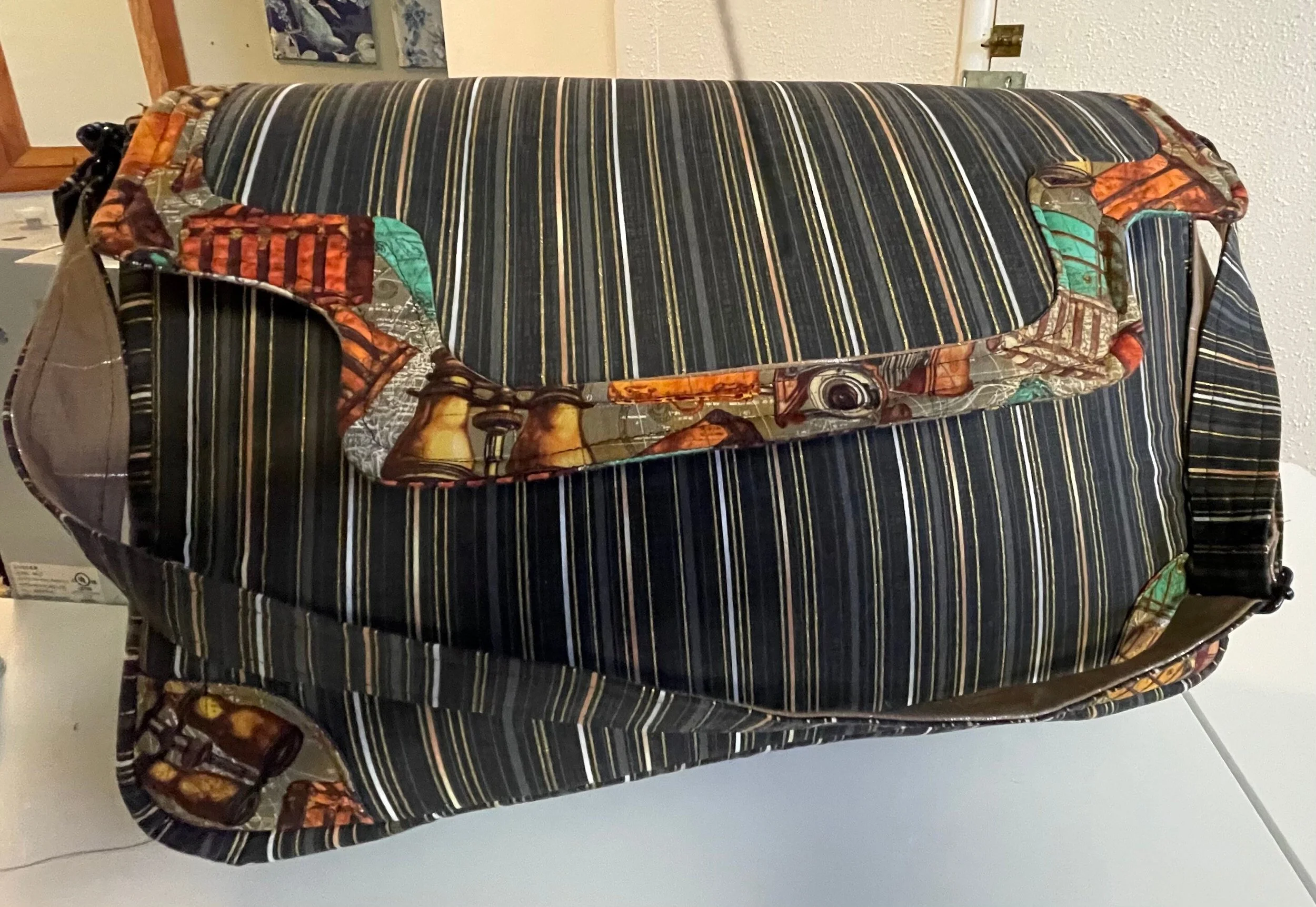 A close-up of a rolled-up quilt with various colorful patterns, placed on top of a striped blanket with black, brown, and beige lines.