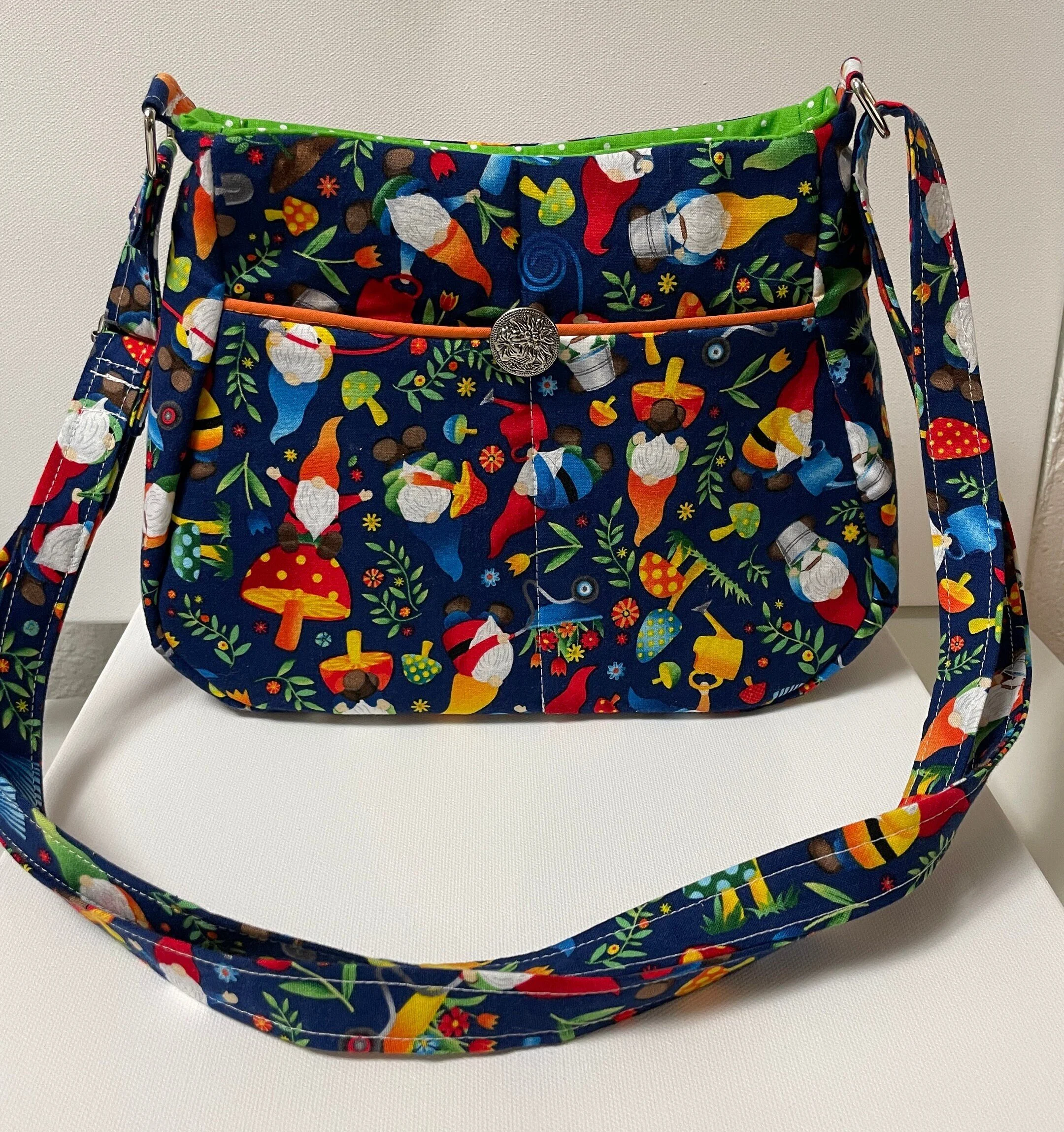 Colorful fabric shoulder bag with gnome and mushroom pattern, metal button closure, and green accents.