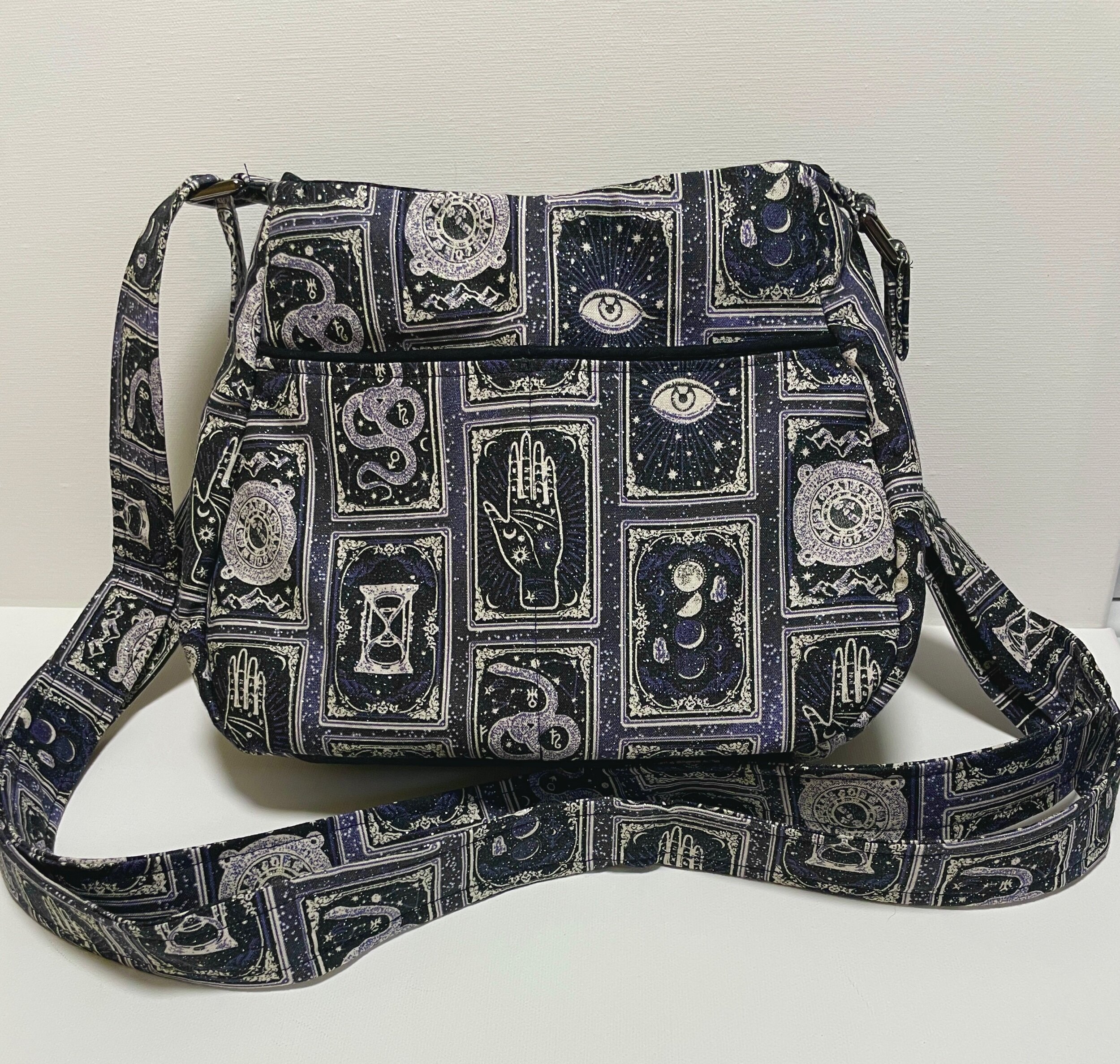 Black shoulder bag with celestial and mystical tarot card designs in white and purple.