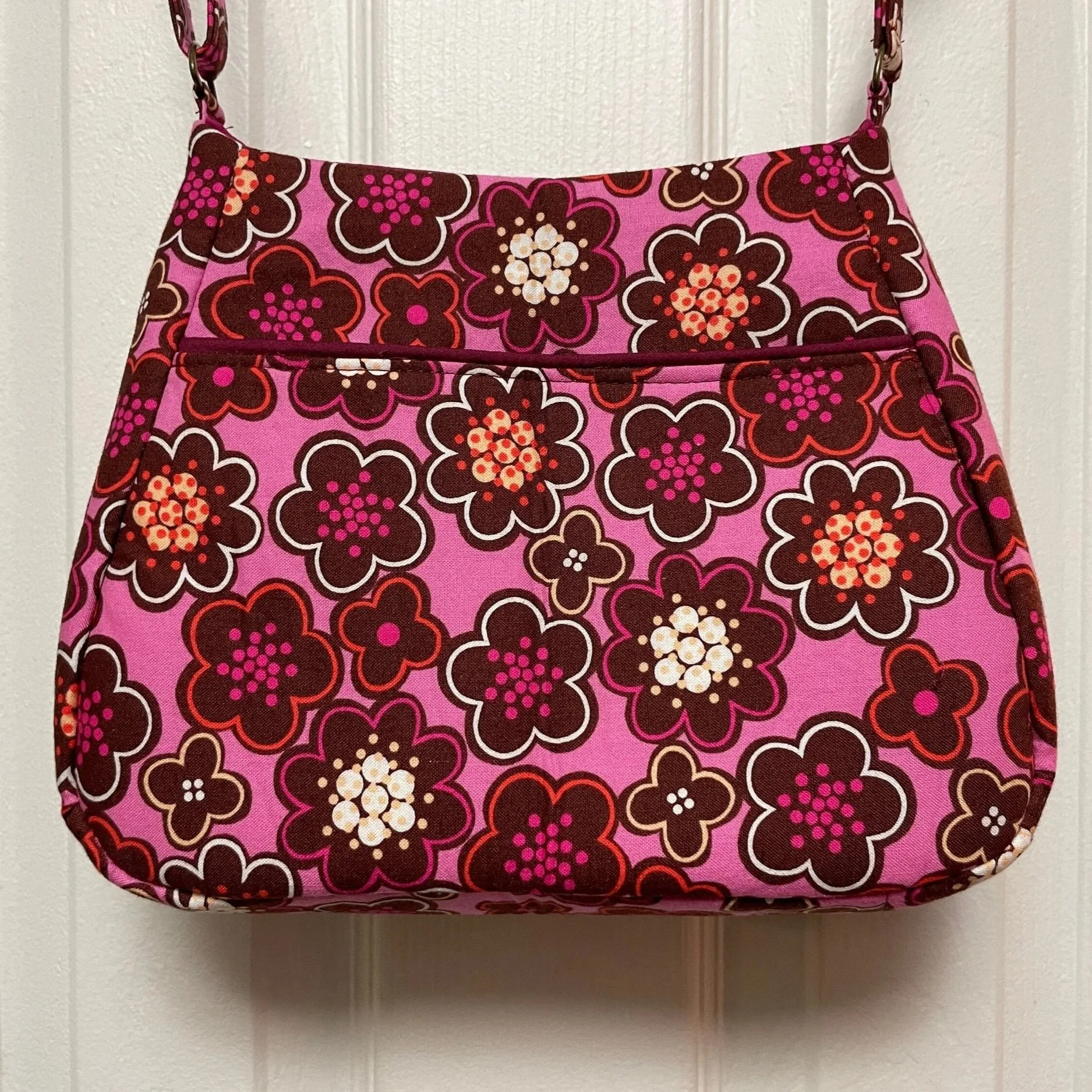 Pink floral-patterned handbag with a zippered pocket hanging on a wall.