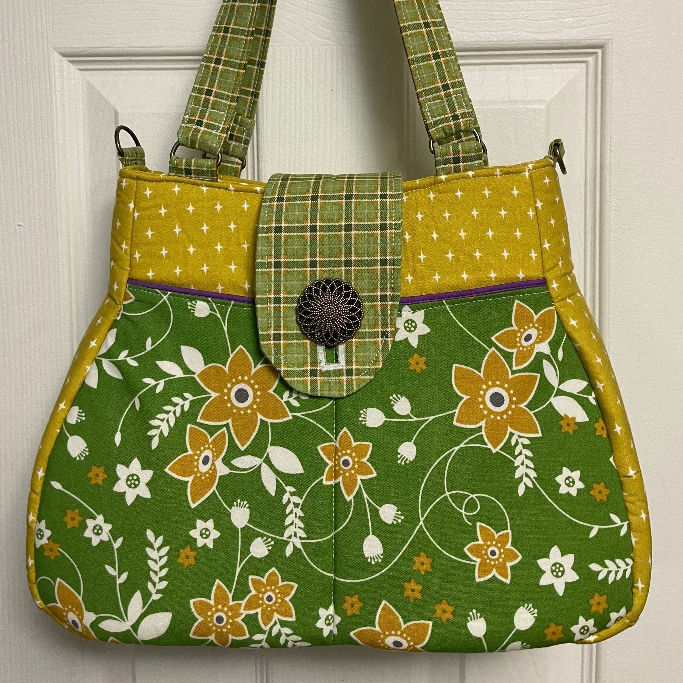 Colorful quilted tote bag with green, yellow, and floral patterns hanging on a white door.