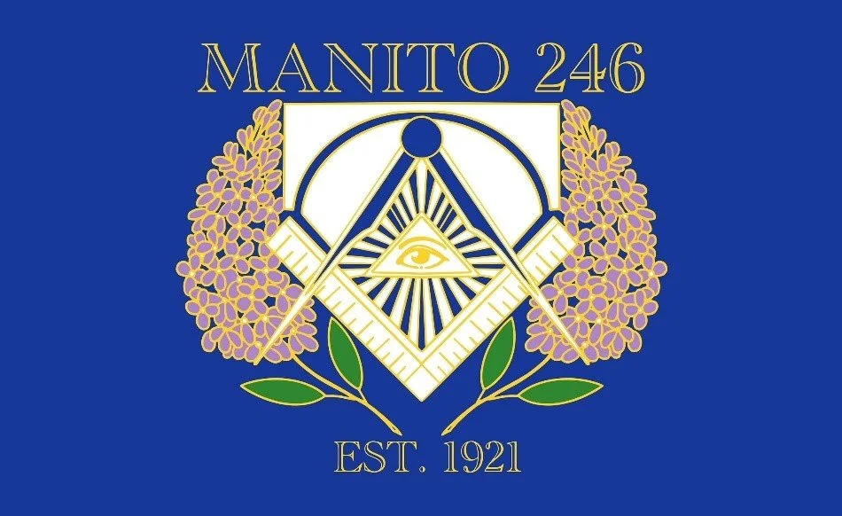 A Masonic emblem featuring a square and compass with a single eye inside a triangle, surrounded by purple flowers, on a blue background. The text reads 'Manito 246' at the top and 'Est. 1921' at the bottom.