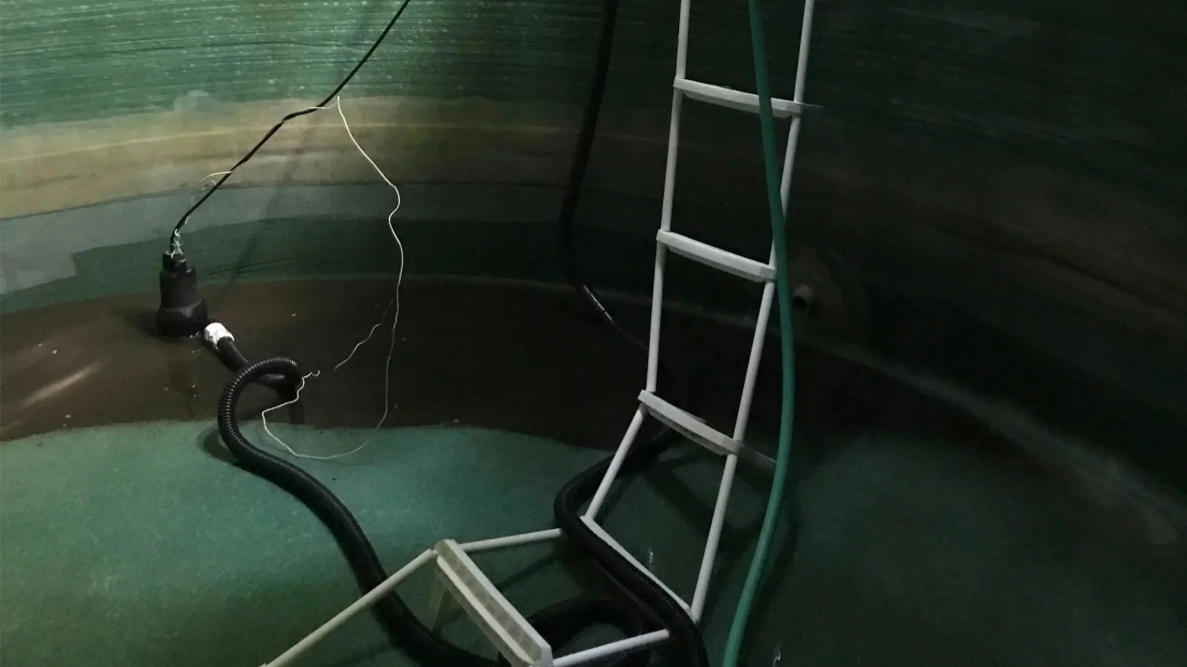 Inside a rainwater tank being throughly cleaned there is a black pump connected to a hose, and dirty water being taken out.