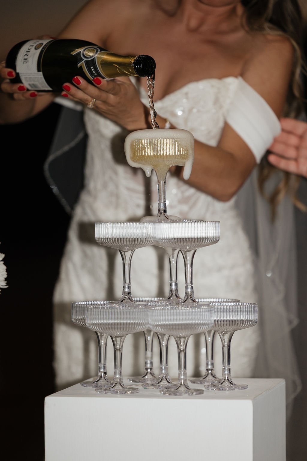 Bride and groom pouring champagne over a tower of coupe glasses at their wedding reception, featuring elevated wedding rentals in the Outer Banks