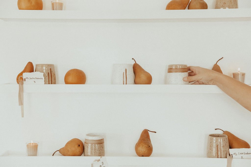  A person holding a candle on a decorative shelf with pears and seating chart. 