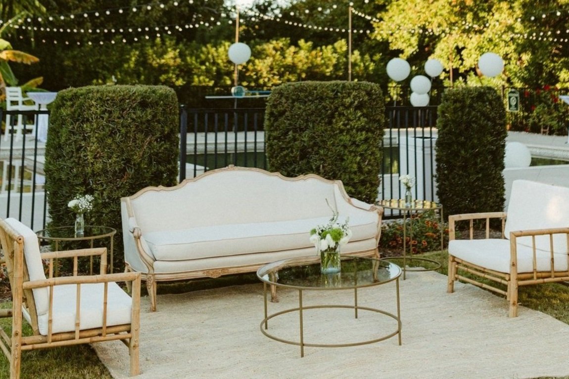  An outdoor lounge collection with white sofa and chairs and string lights at OBX event venue. 