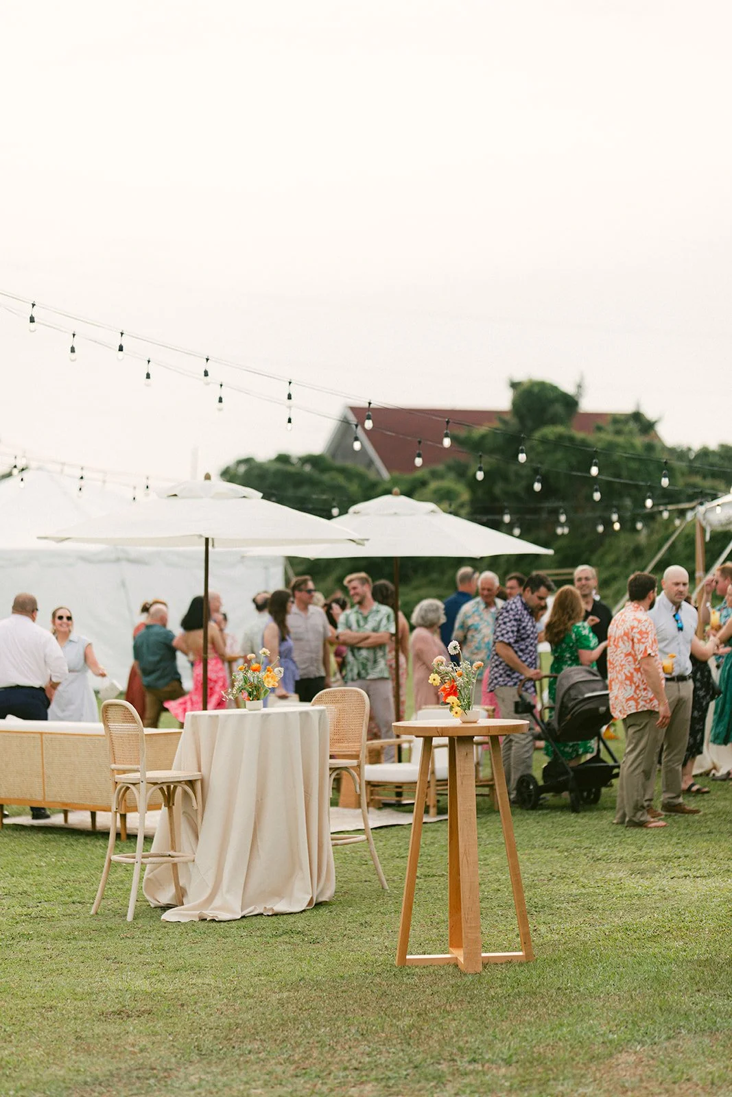 Outdoor wedding reception with cocktail tables, rattan bar stools, and a white lounge setup, showcasing curated event rentals by Amaranth + Artifact