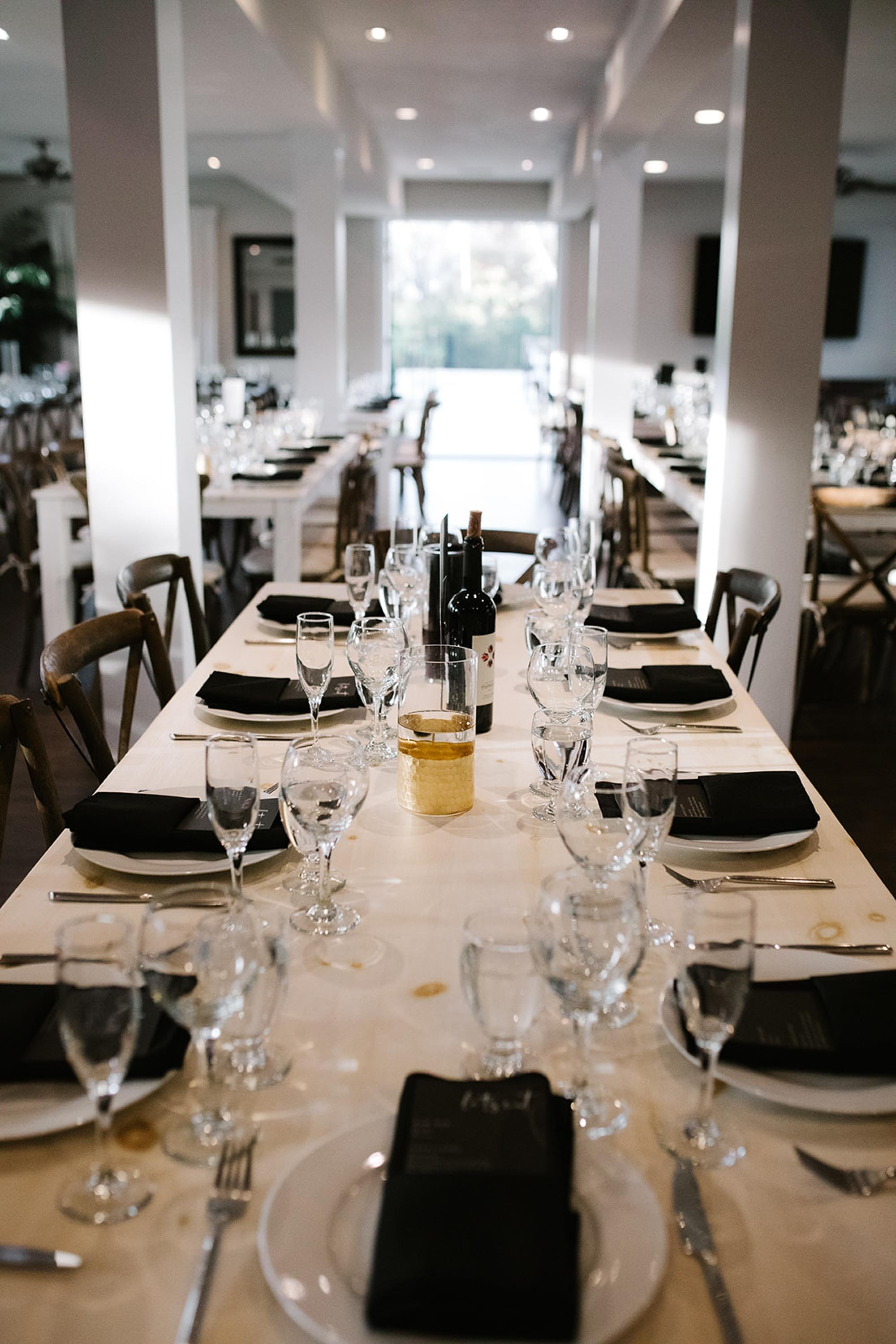 Long wedding reception dining tables with black napkins, custom menus, and glassware rentals