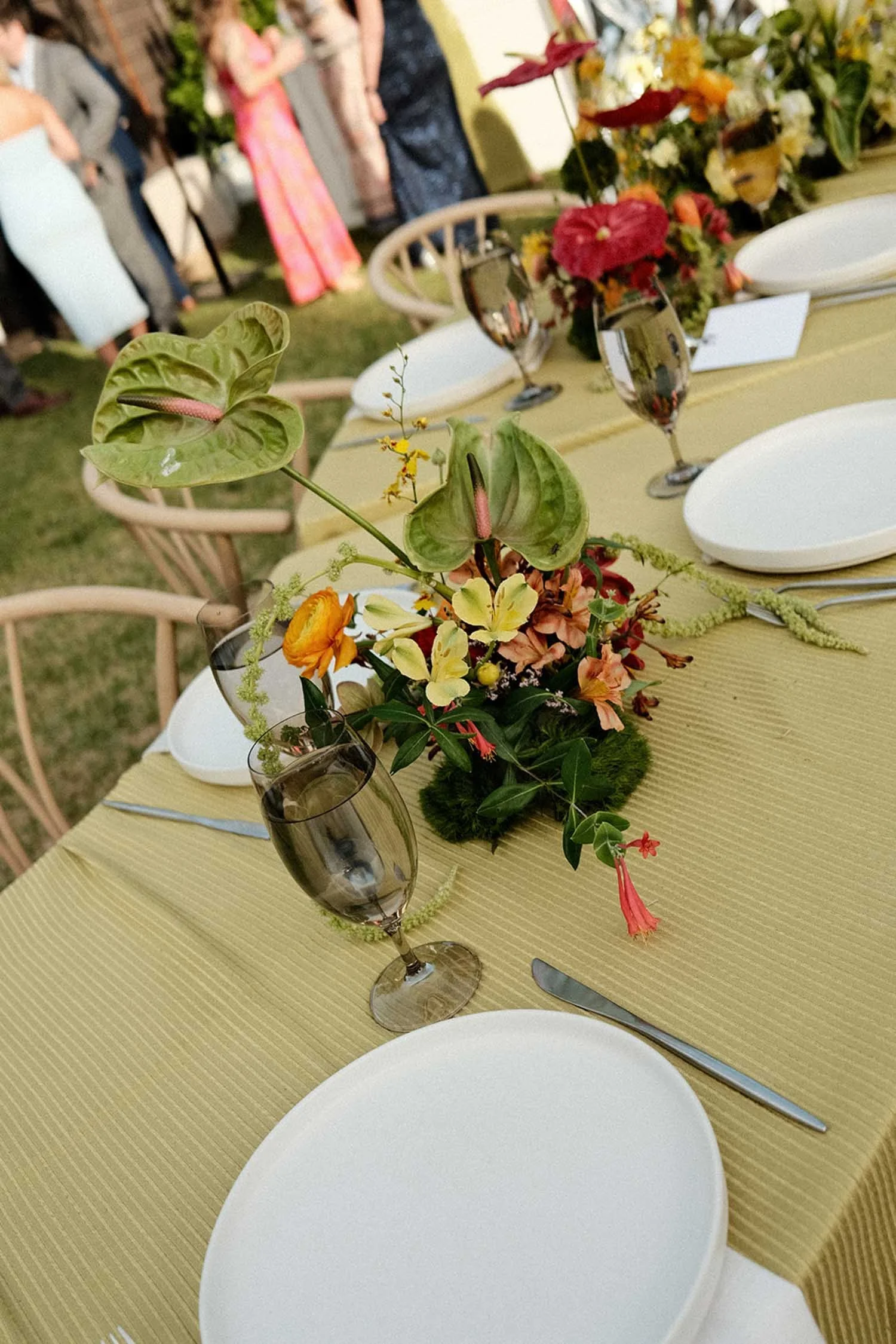 Tabletop with a unique floral arrangement, green ribbed tablecloth, smoky gray glassware, and modern white plates, showcasing Amaranth + Artifact tabletop rentals