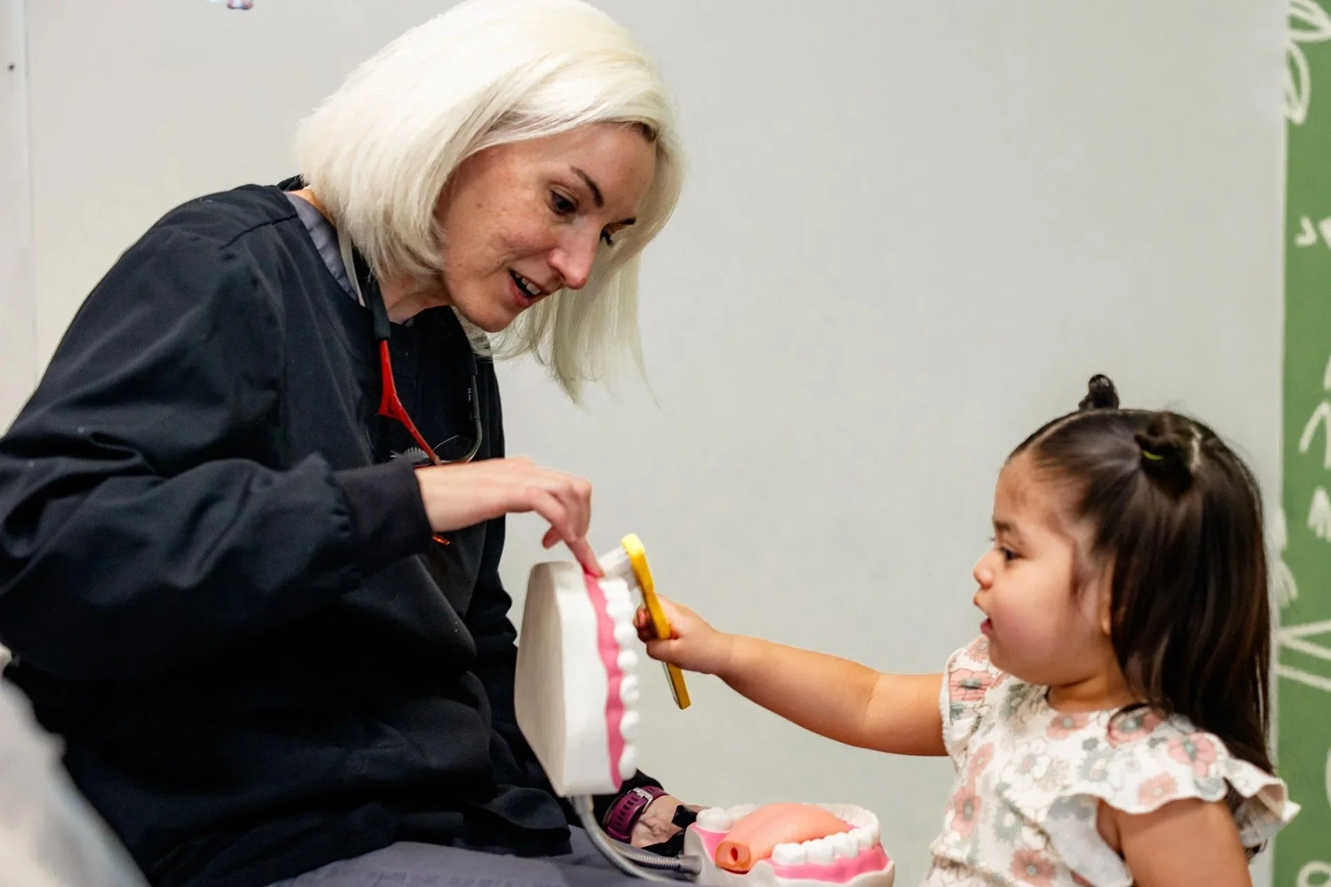 A young girl learning to brush teeth with a dentist in scrubs.