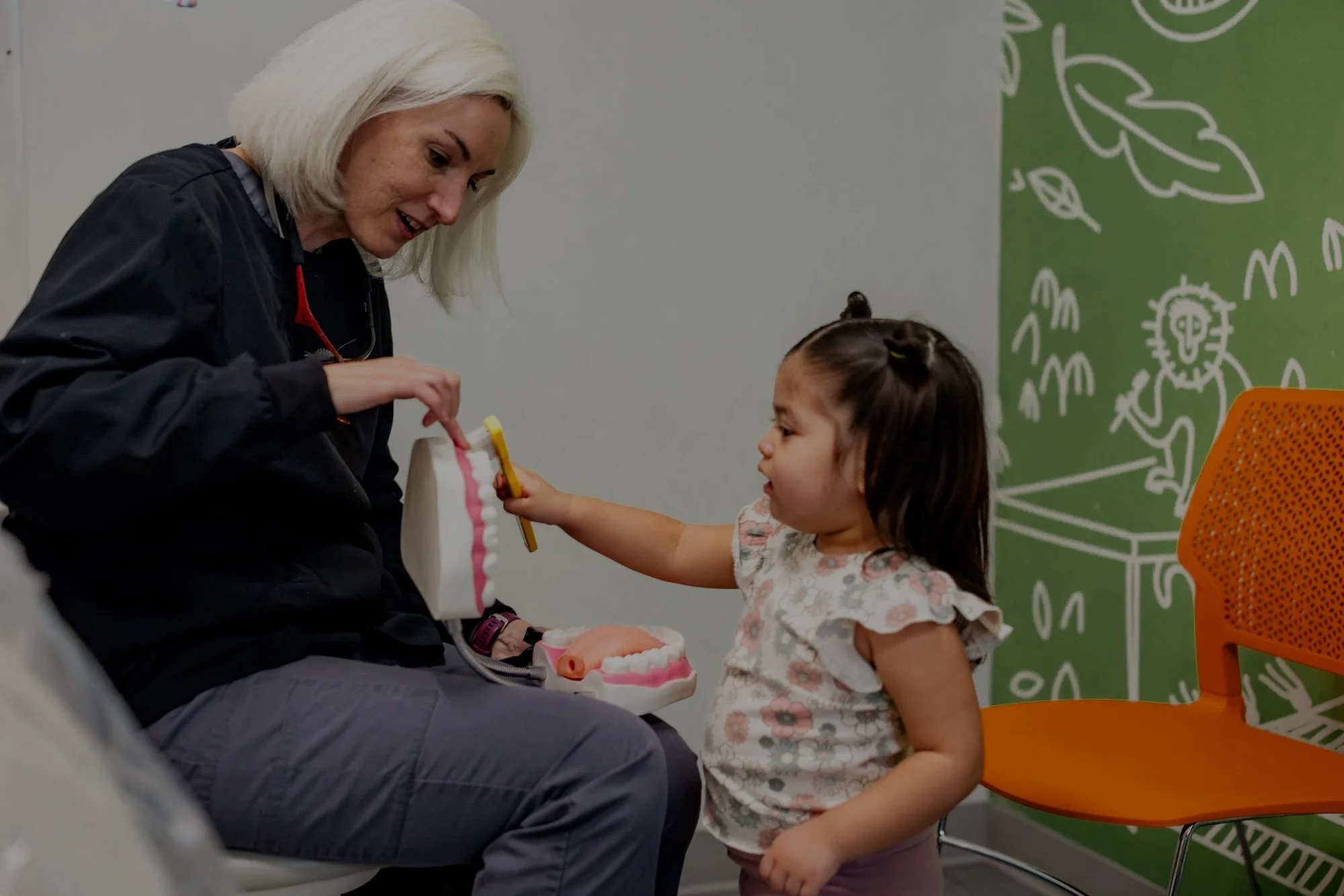 A young girl learning to brush teeth with a dentist in scrubs.