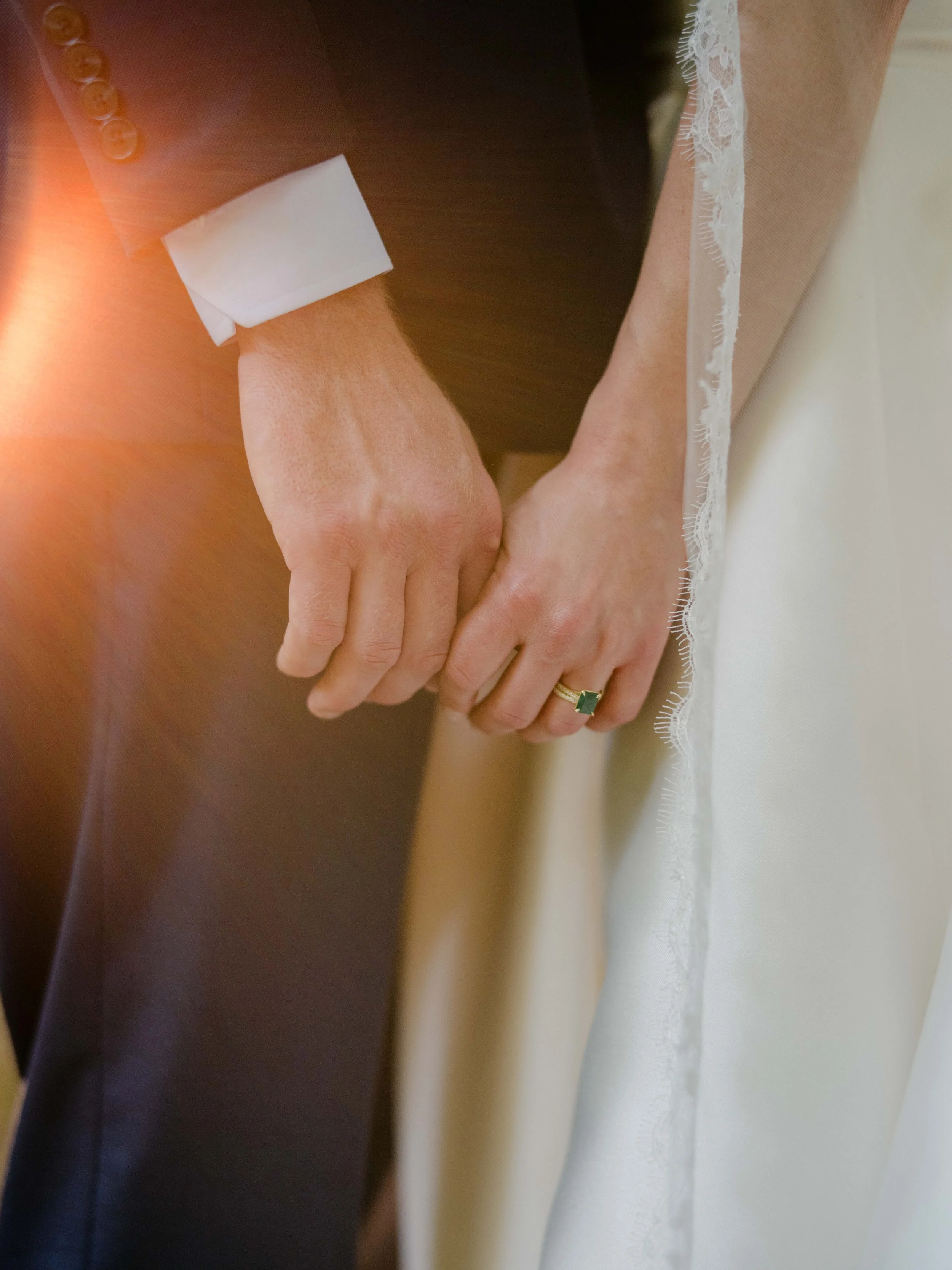 Close-up of a couple holding hands, with the bride wearing a wedding ring, during a wedding ceremony.