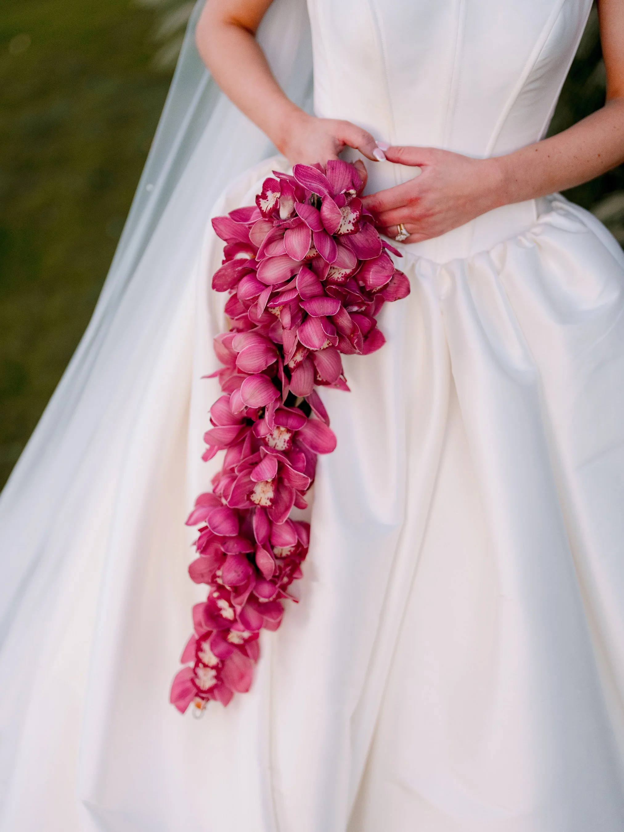 Bride holding a cascading pink orchid flower bouquet on her wedding dress.