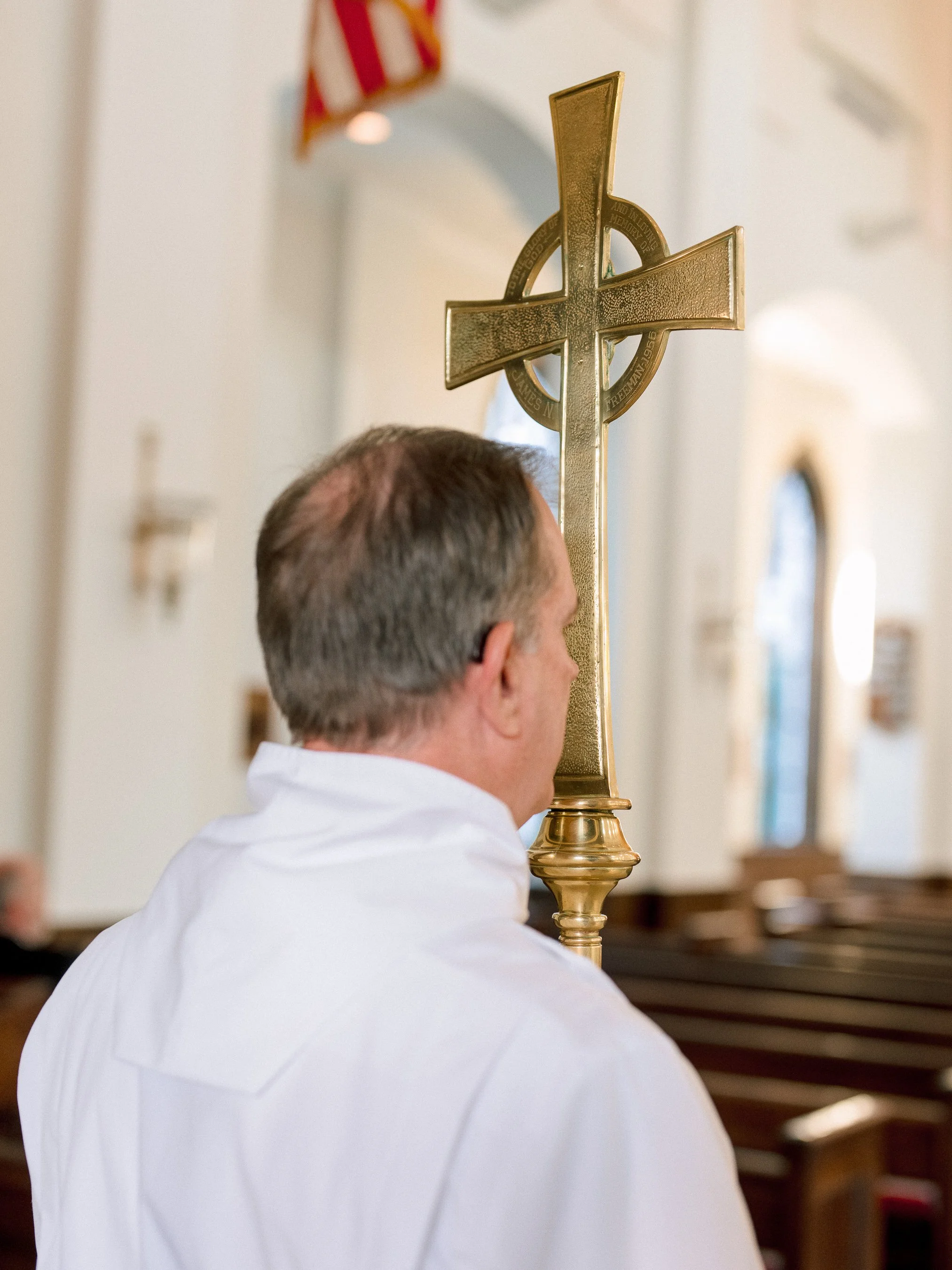 A man in a white shirt holding a large gold cross during a religious ceremony inside a church.