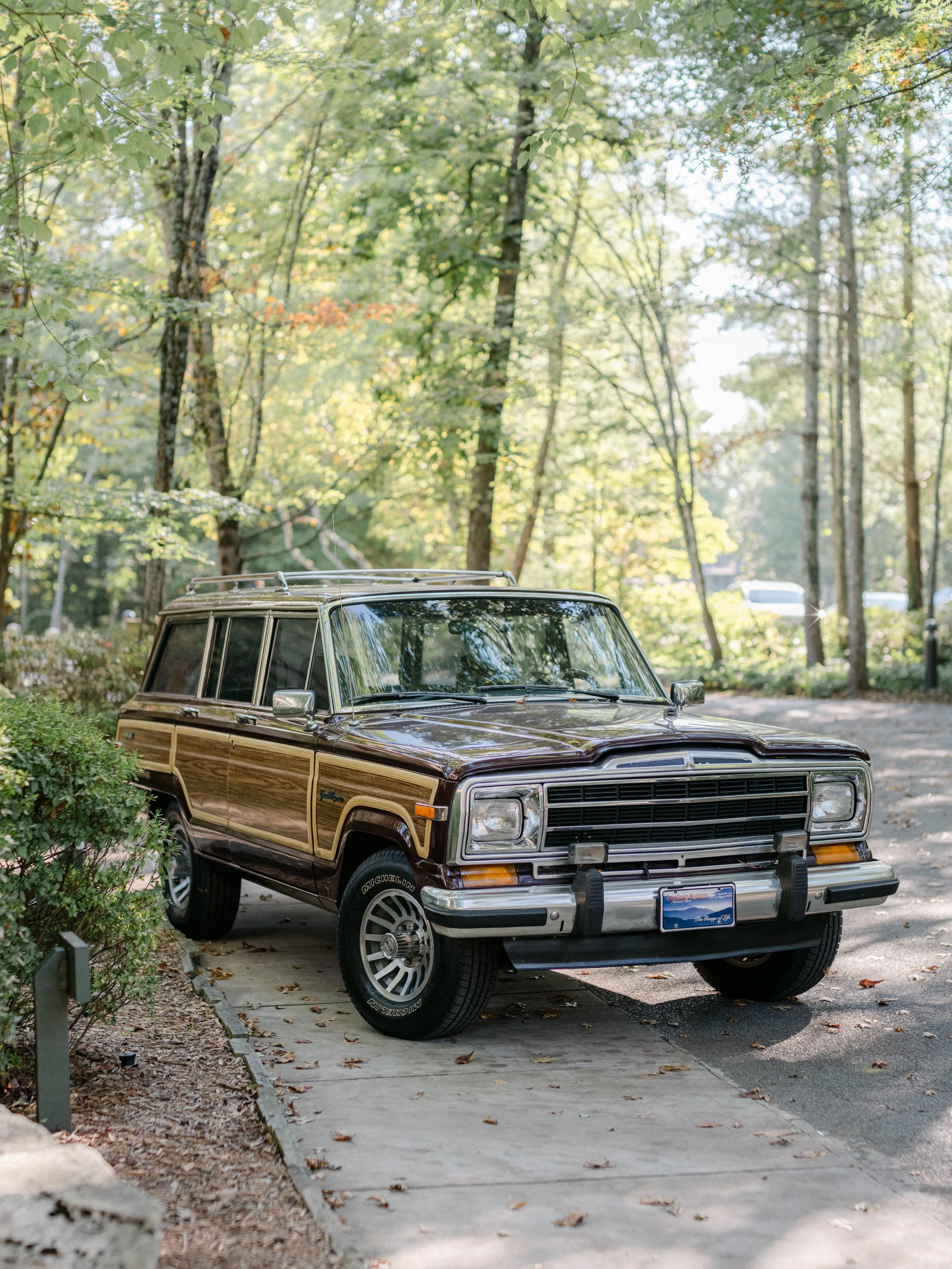 A vintage Jeep Cherokee parked on a small driveway surrounded by trees and greenery.