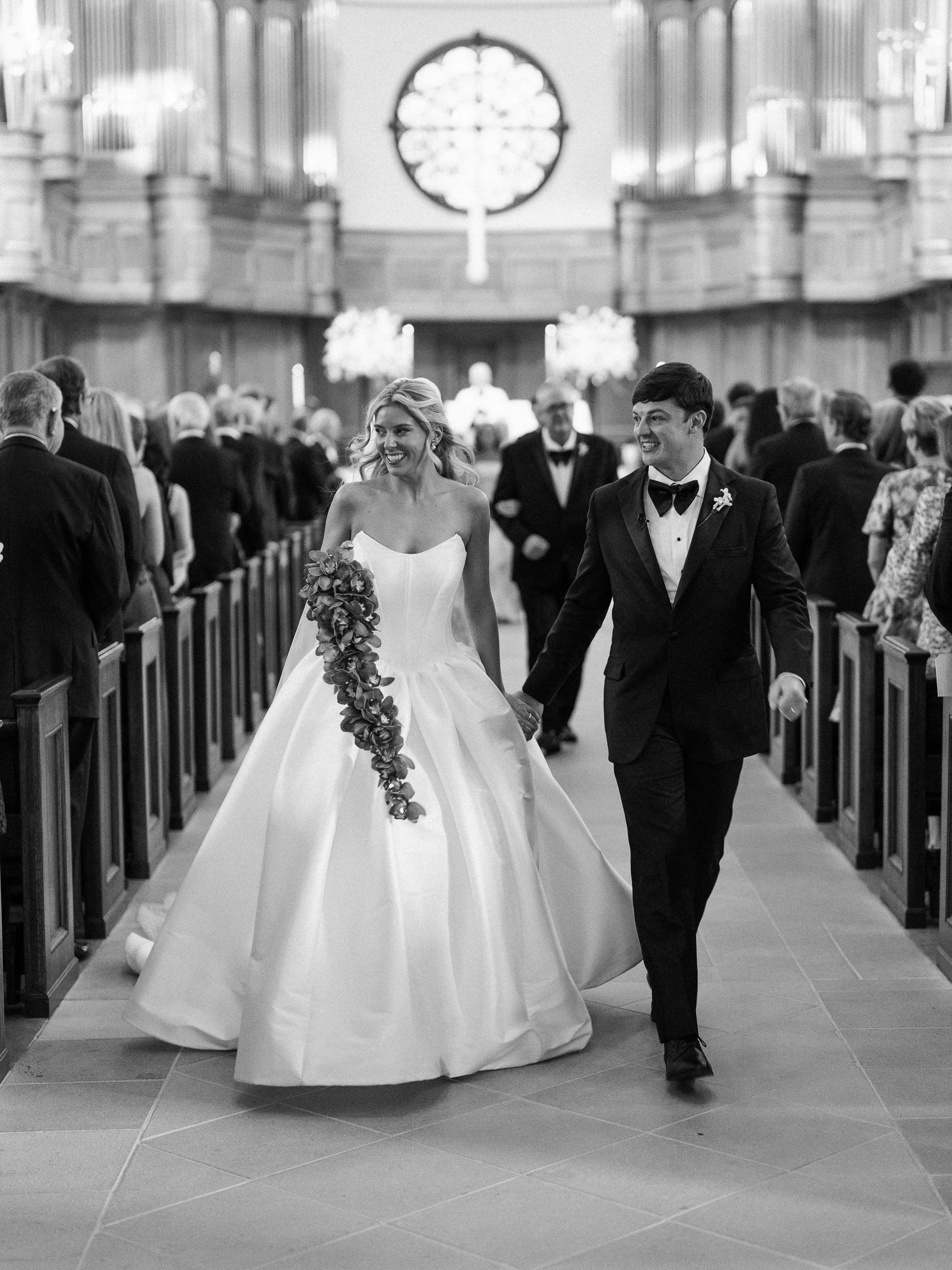 A bride and groom walking hand in hand down the aisle of a church during their wedding ceremony, surrounded by guests.