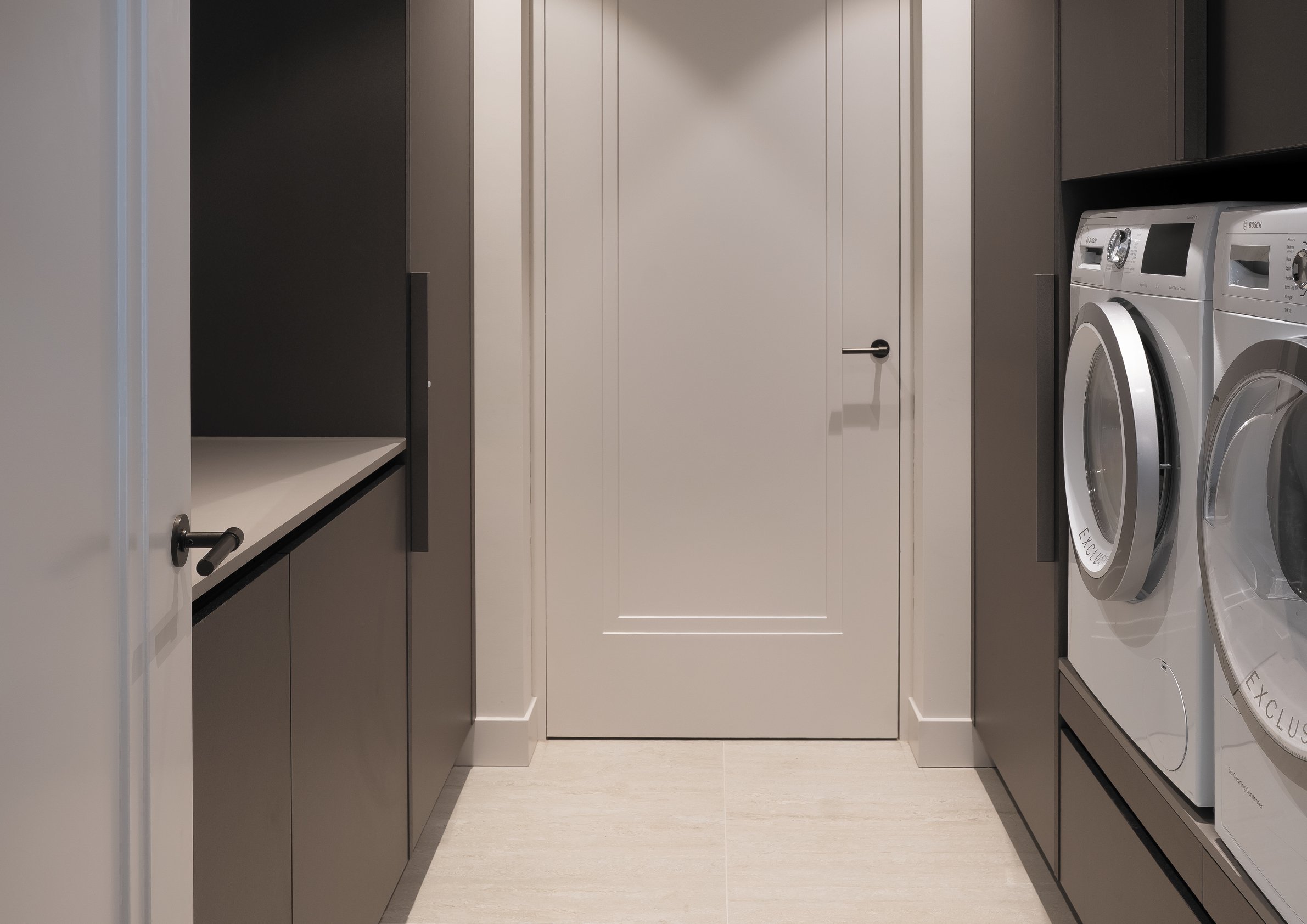 Een wasruimte met een witte deur in het midden, omgeven door kasten en wasmachines met deursloten aan de rechterkant.