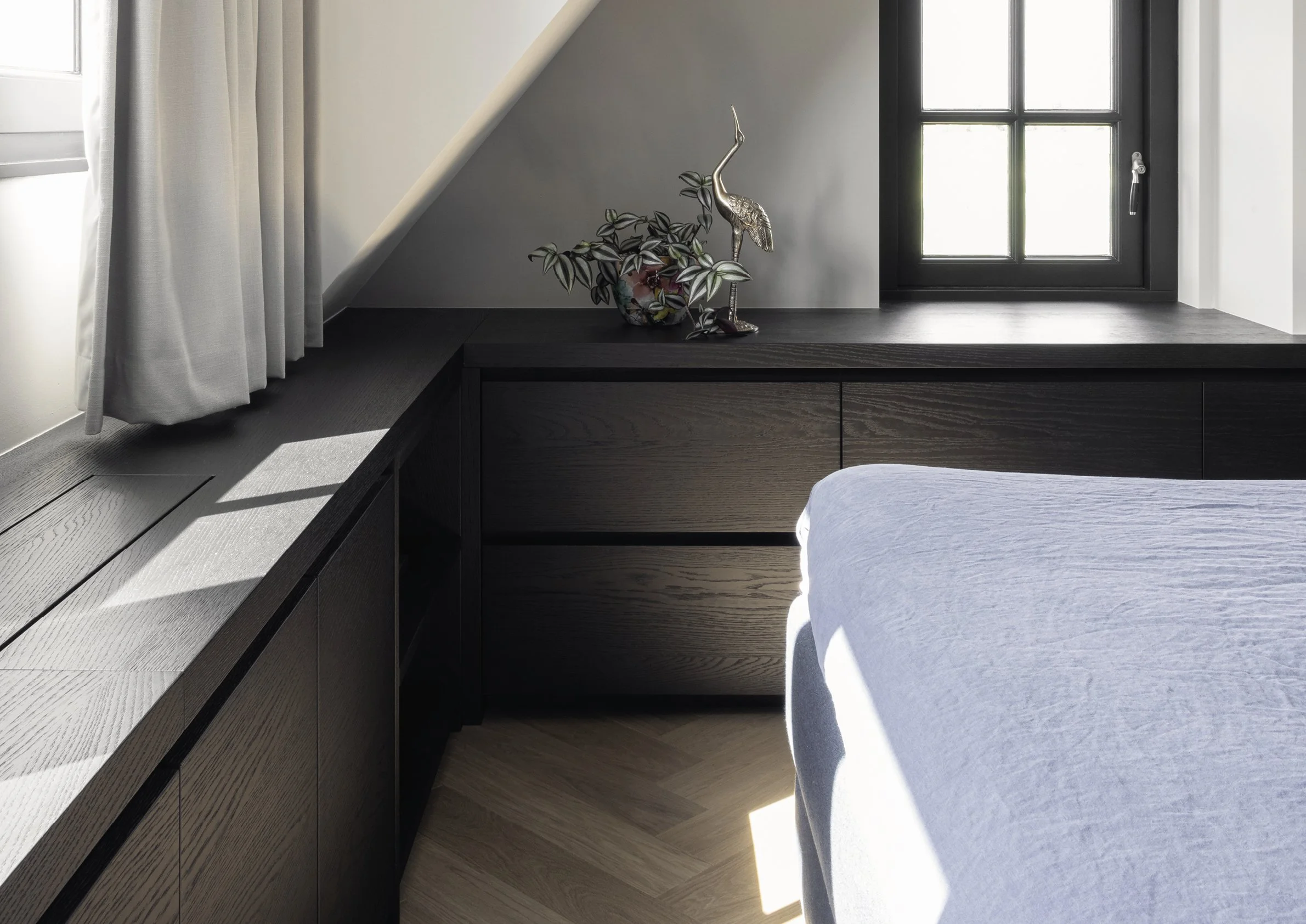 Gedekte slaapkamer met zwart meubel, een raam en decoratieve items zoals een plant en een beeld van een flamingo.