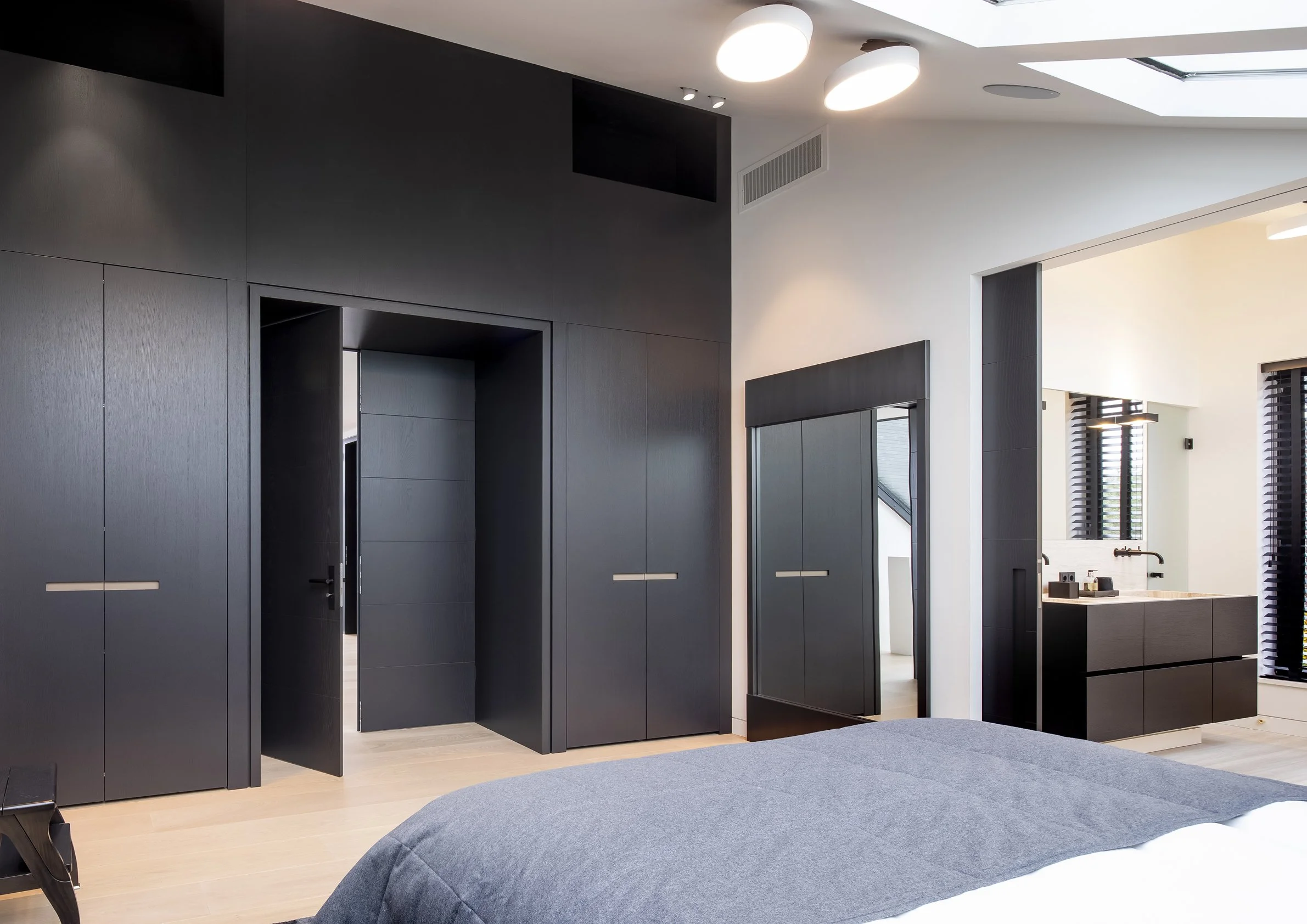 Moderne slaapkamer met zwart wandmeubels, spiegel en badkamer met wastafel en zwarte afwerking.