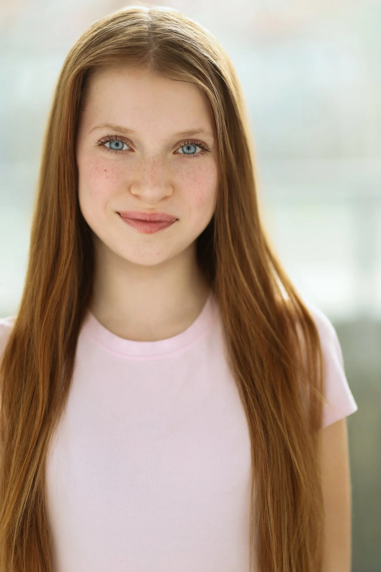 A young girl with long curly red hair and blue eyes, smiling in front of a blue Acura car.