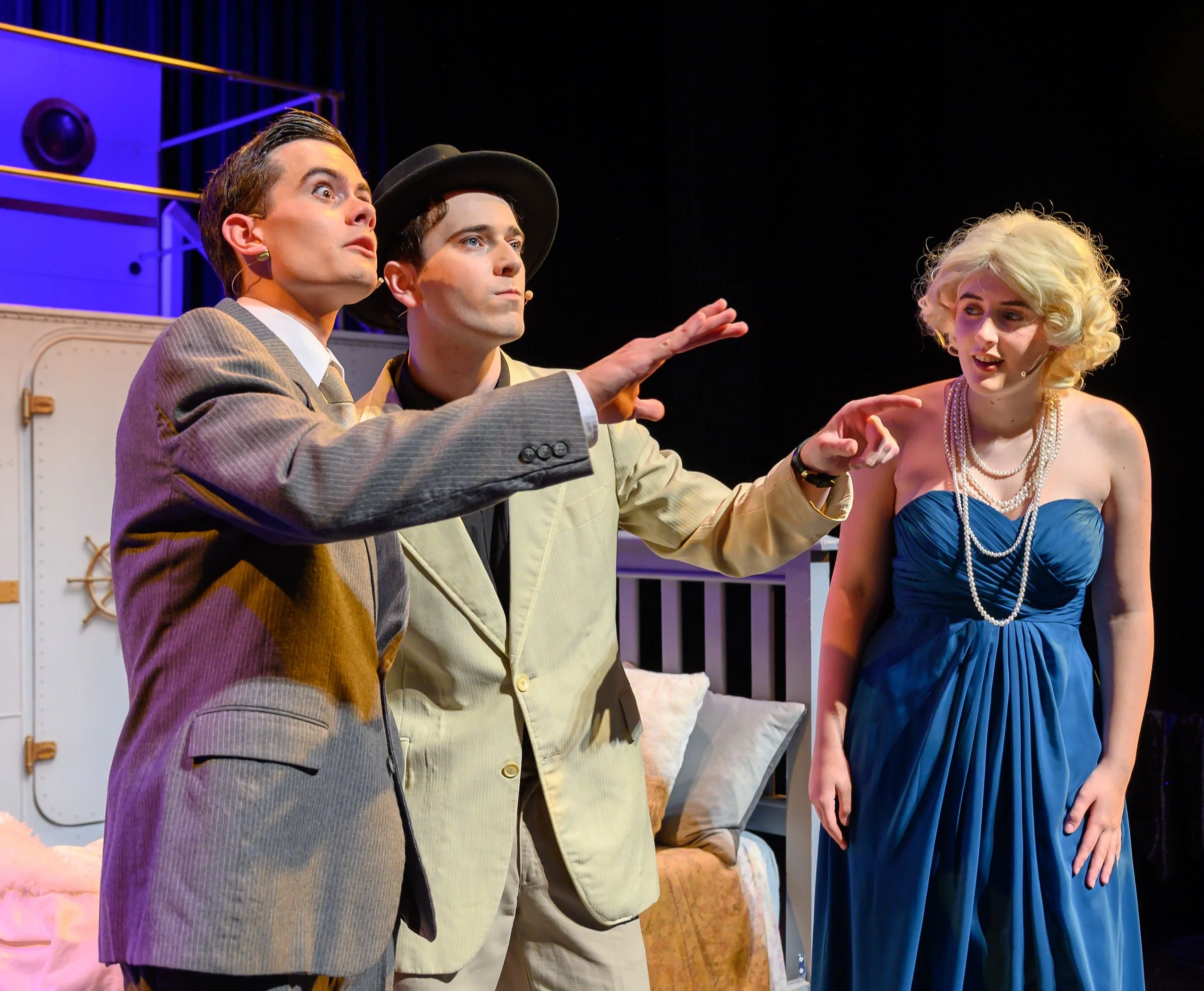 Four people on stage, three men and one woman, all dressed in vintage clothing, engaged in a theatrical performance with expressive gestures.