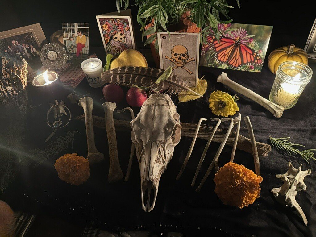 A Halloween altar with candles, a skull, bones, flowers, apples, Halloween-themed decorations, and photos.