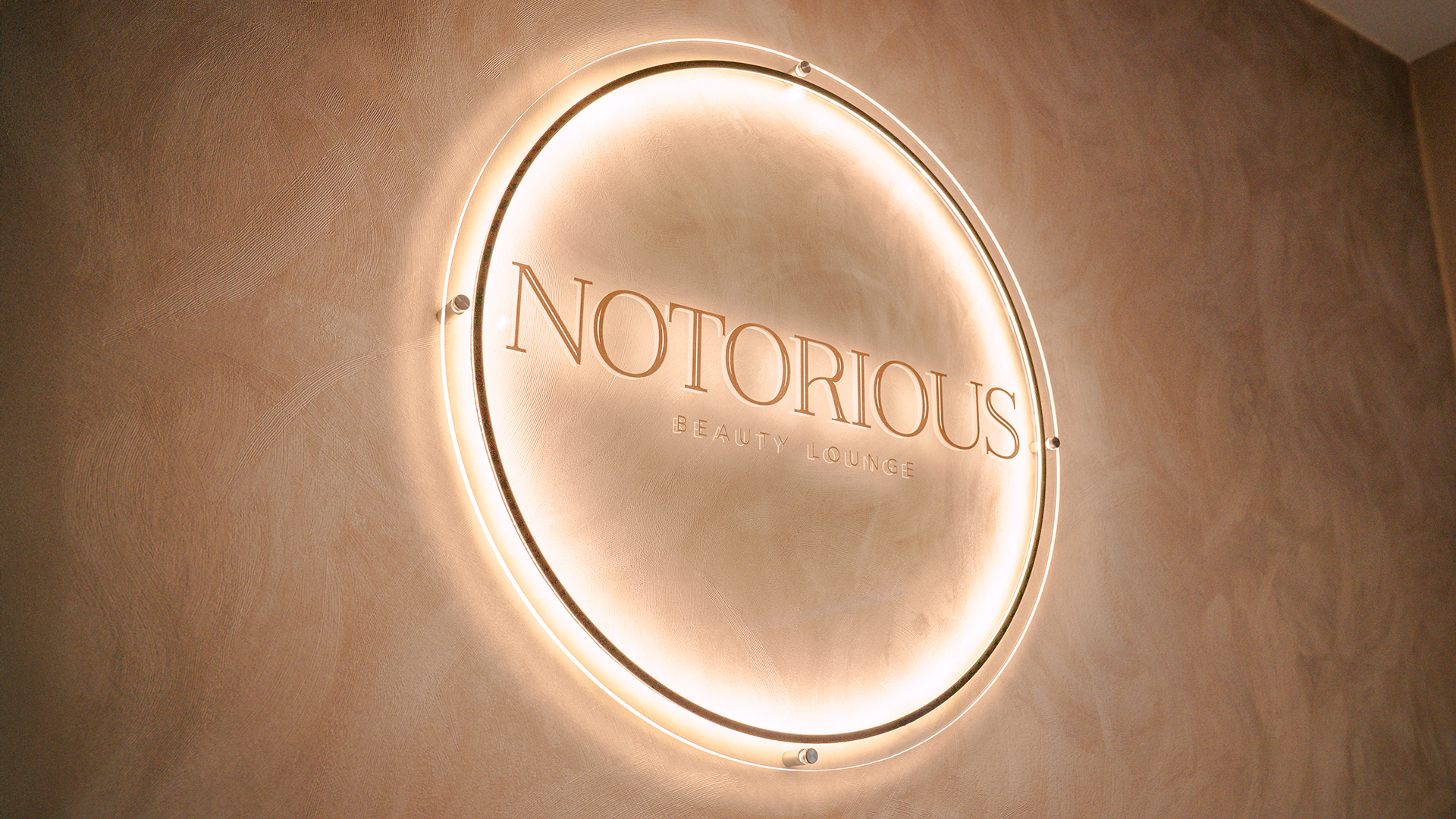 Neon sign reading 'Notorious Beauty Lounge' on a beige wall.