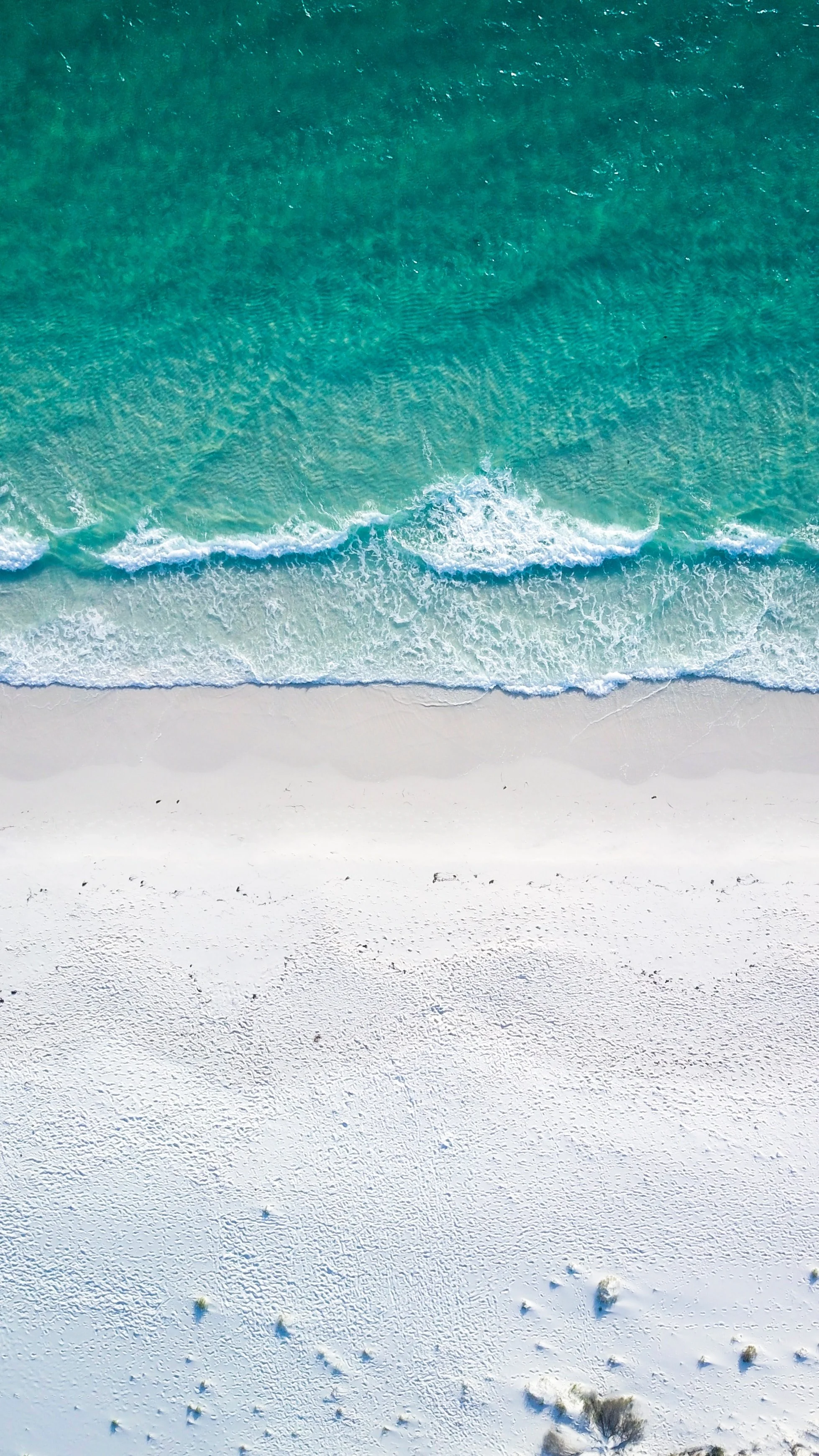 Aerial view of a beach with white sand, turquoise water, and gentle waves.