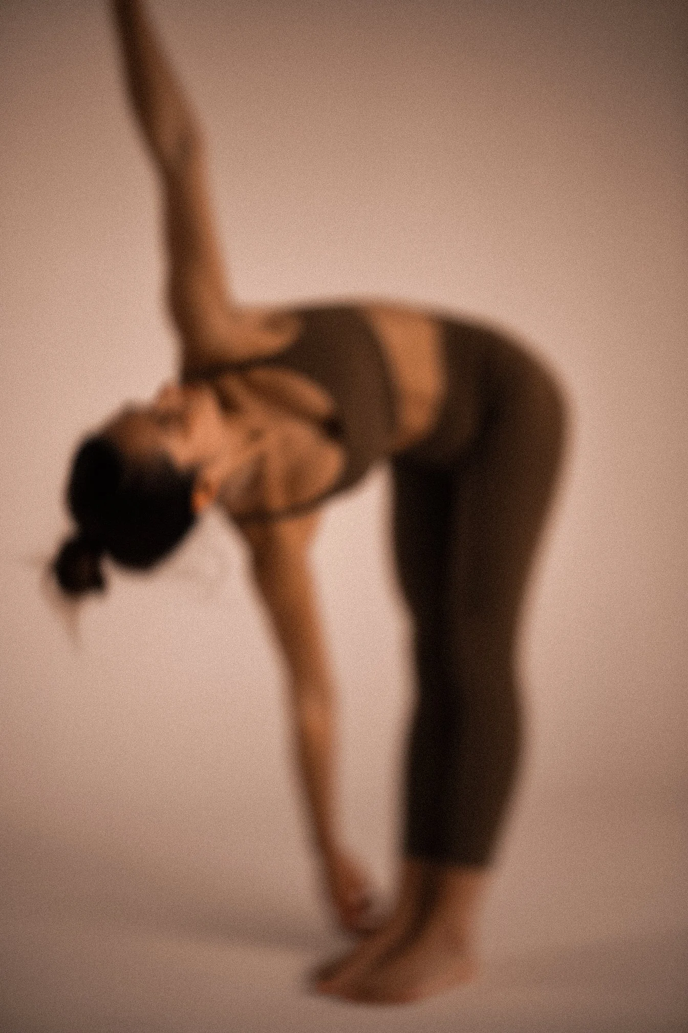 A woman performing a yoga pose, bending forward with one arm extended overhead and the other hand reaching towards her foot, in a studio setting.